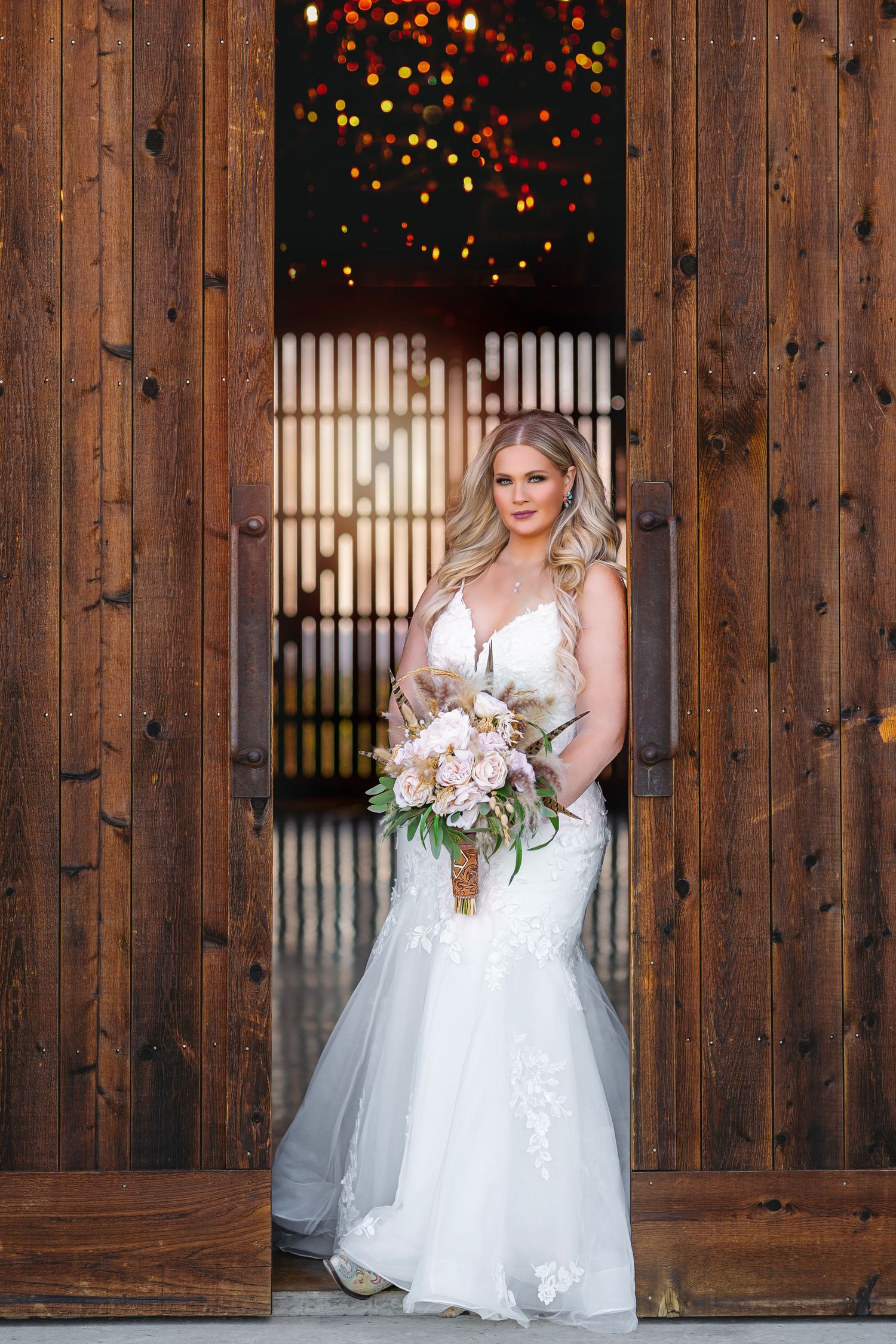 Bride in white dress poses against wooden wall with twinkling holiday lights.