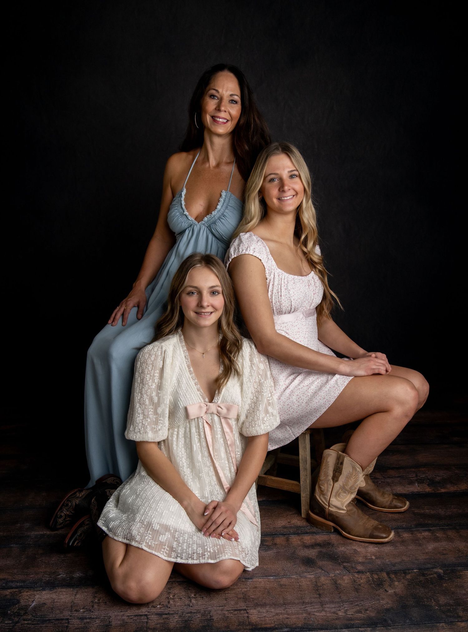 Professional studio portraits against black background showcase subjects in white dresses and boots with rustic styling.
