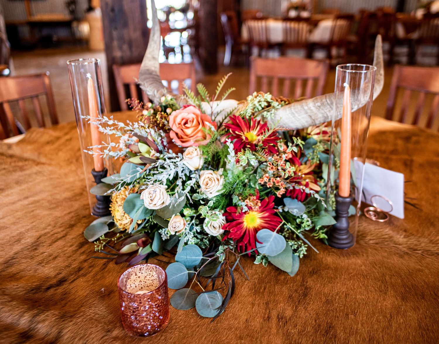 Elegant floral centerpiece with roses and eucalyptus leaves surrounded by glass candleholders on wooden table.