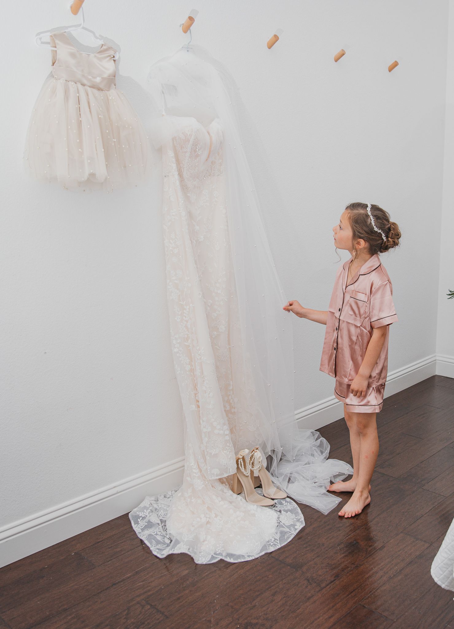 A wedding dress and flower girl dress hanging on display with a child looking up in admiration.