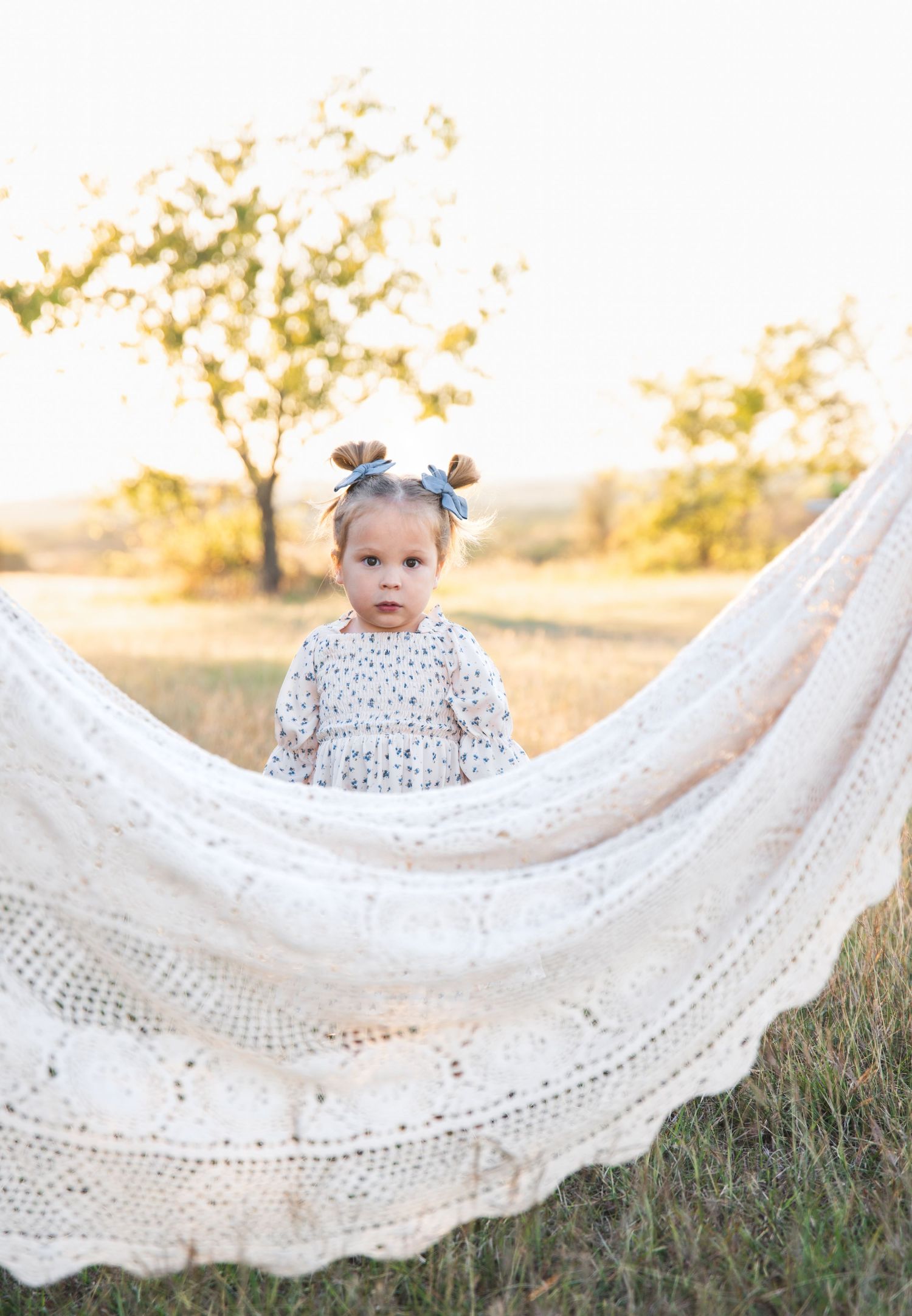 A delicate white lace blanket is displayed in a grassy field with warm sunset lighting.
