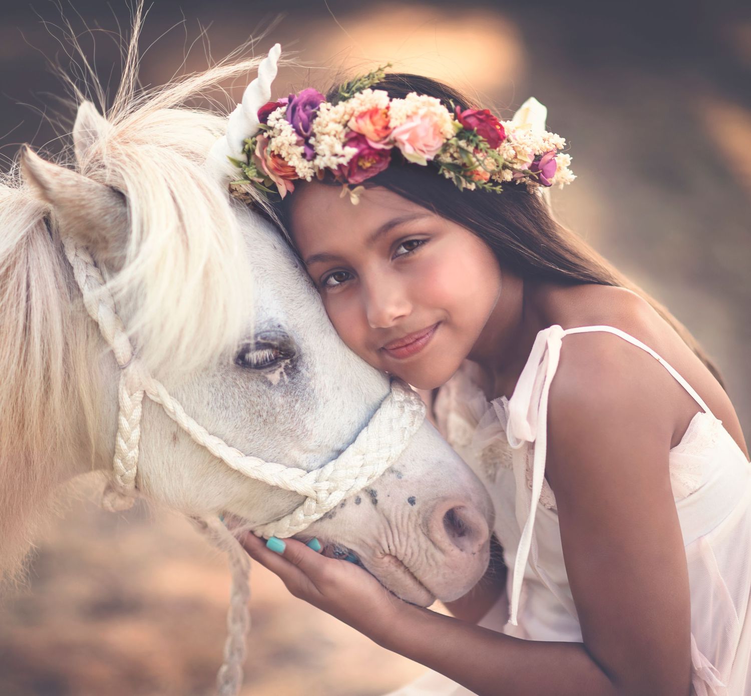 Dreamy portraits with a white horse adorned with floral wreaths in soft lighting.