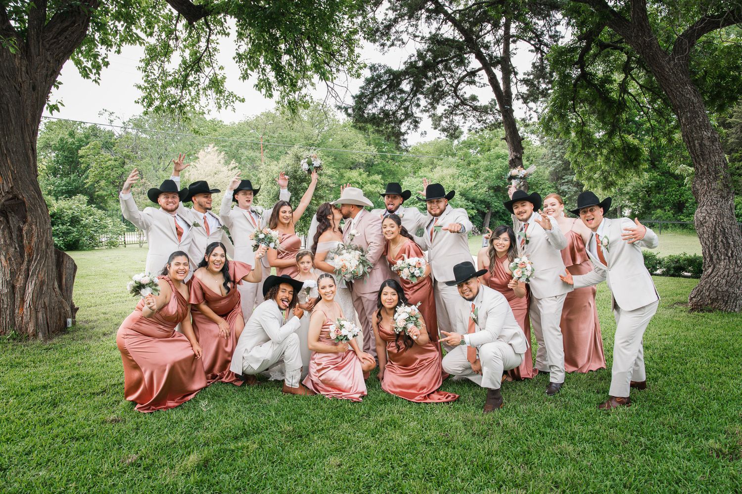 Wedding party poses playfully on a grassy hill in coordinated coral and white outfits.