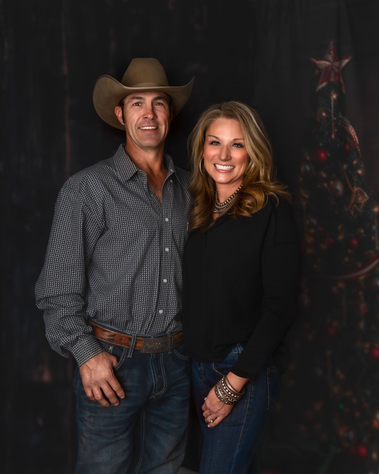 Western-styled couple poses against dark backdrop with Christmas decorations.