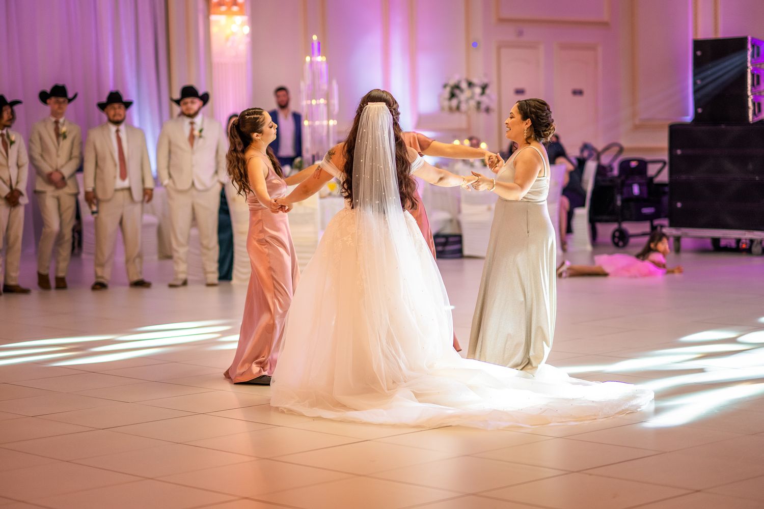 Wedding dance scene with bride in white gown surrounded by guests in pink and white.