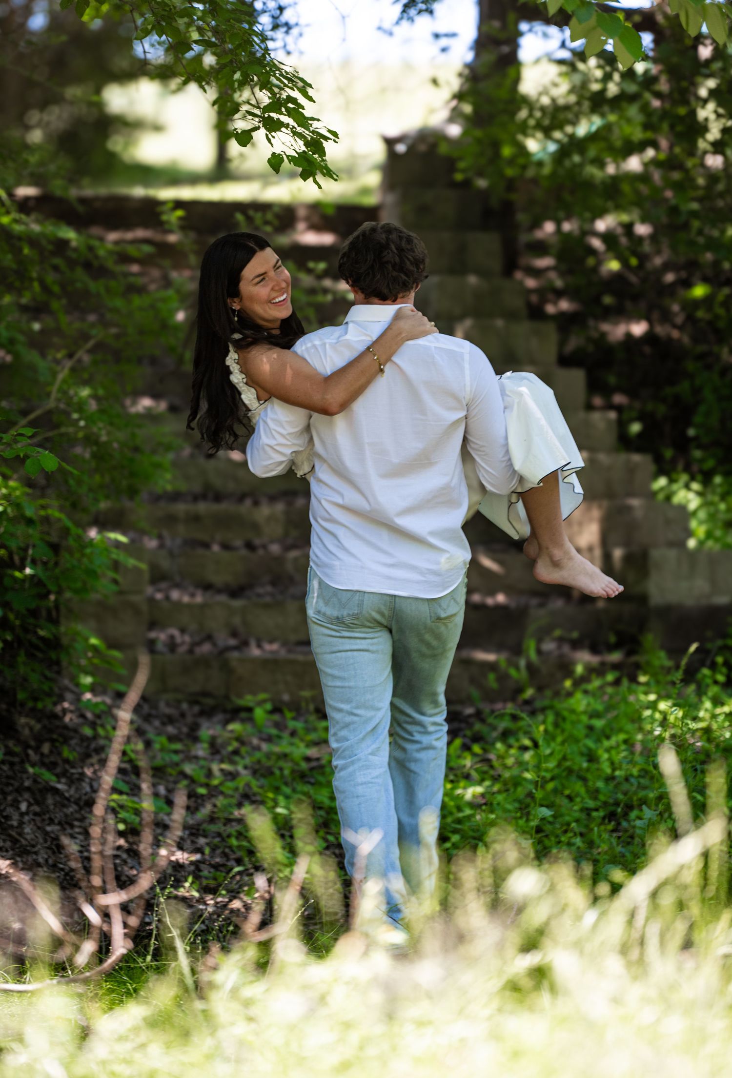 A romantic couple shares an intimate moment on stone steps surrounded by lush greenery in an outdoor setting.