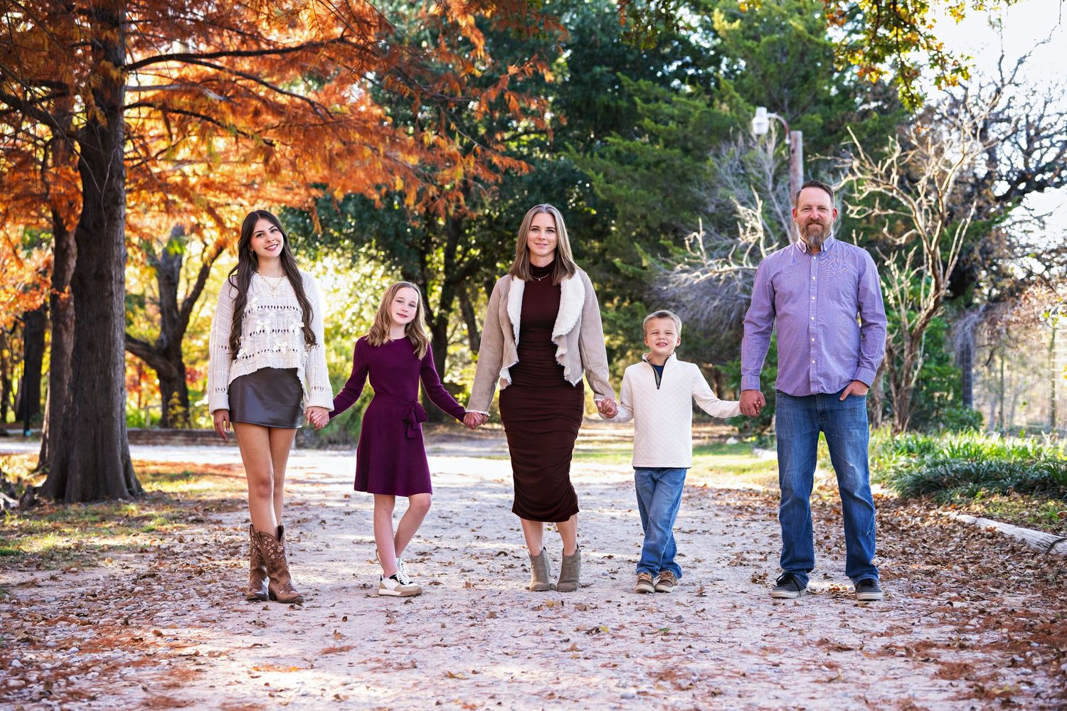 A group of people walking together along a tree-lined path during autumn with warm golden lighting.