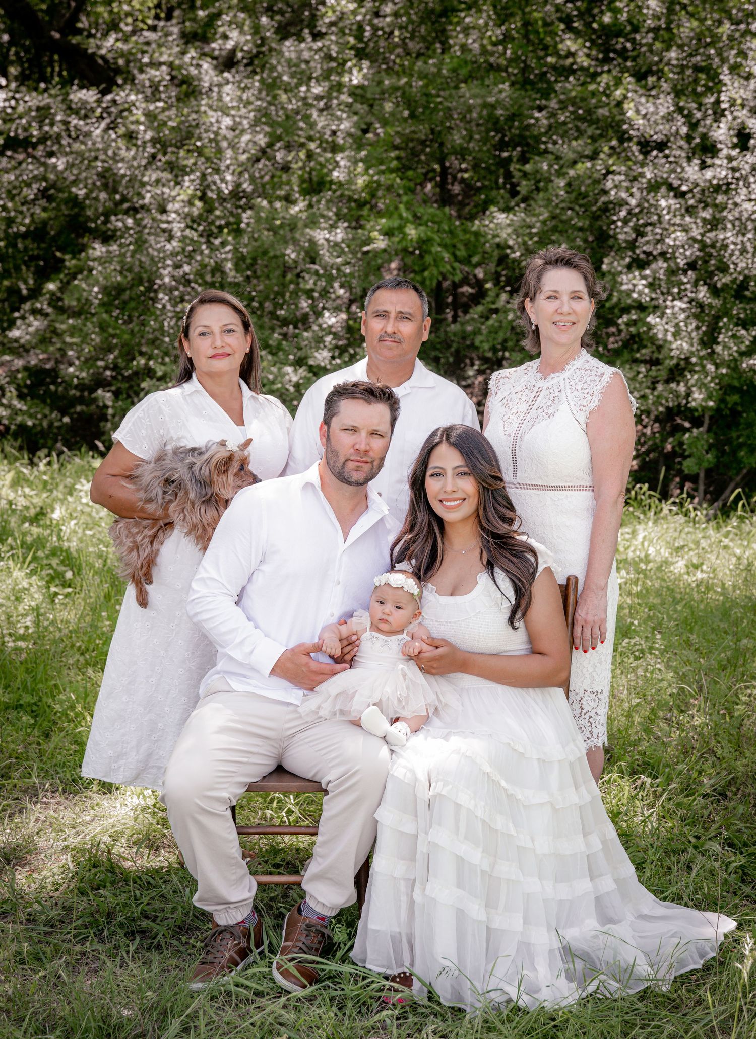 Large family portrait in all white attire posed in blooming spring garden.