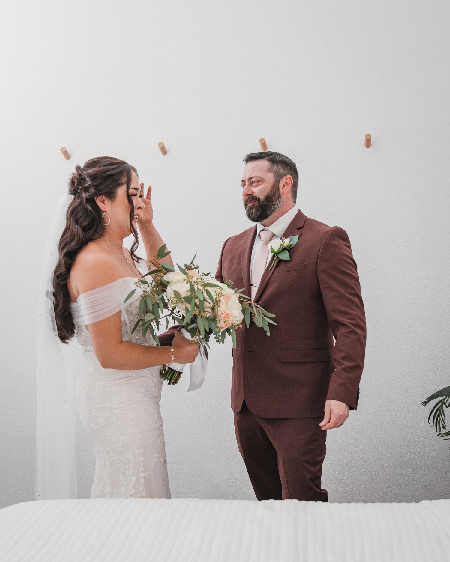 An emotional first look wedding moment captured against a white wall.