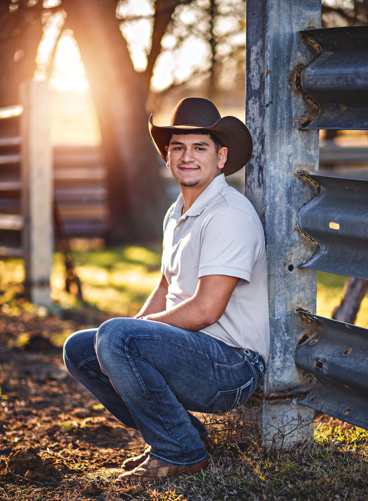 Western style portrait session with cowboy hat near wooden fence at sunset.