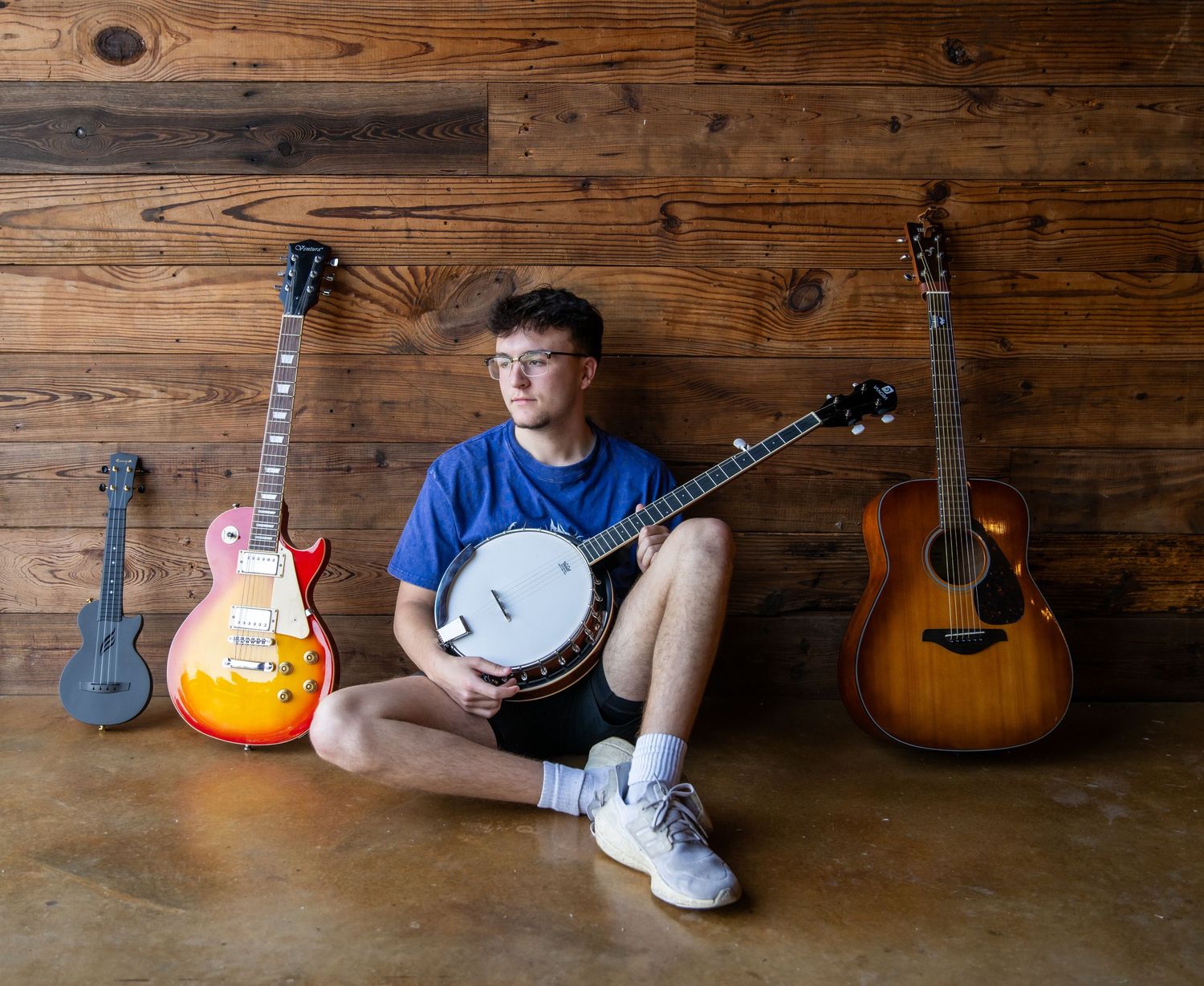 Collection of musical instruments including guitars and banjos arranged along a rustic wooden wall.