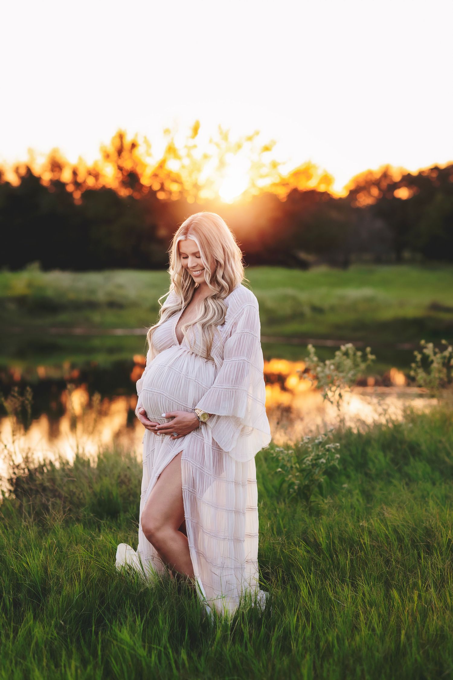 Ethereal maternity photos by lake at sunset in white flowing dress.