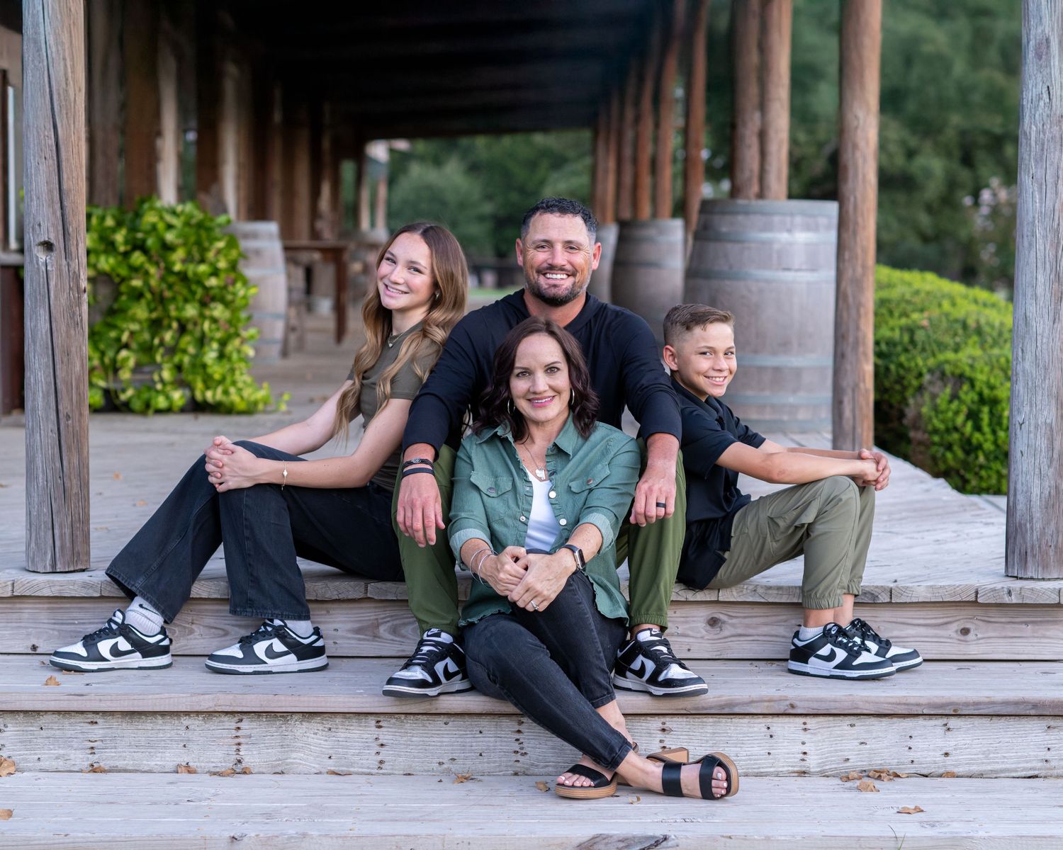 Family sitting together on rustic wooden porch steps during outdoor photoshoot.