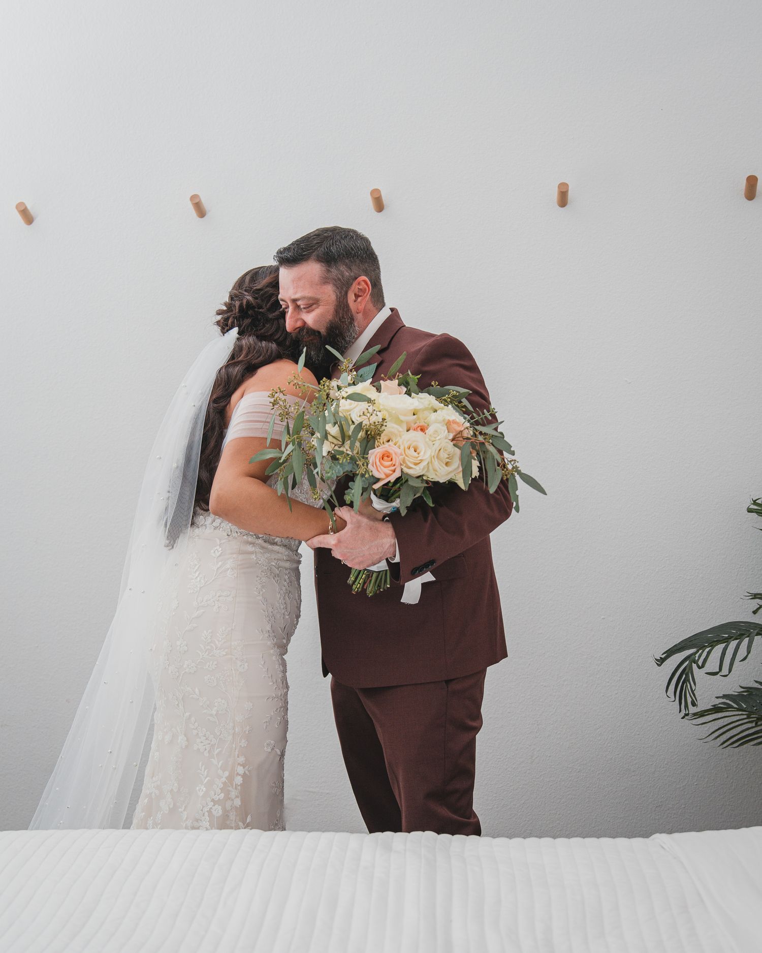 An intimate first look moment between newlyweds against a white wall with a beautiful bouquet.