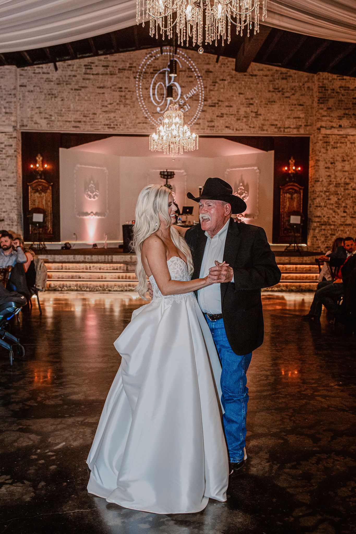 Wedding reception dance in a rustic venue with crystal chandelier lighting.