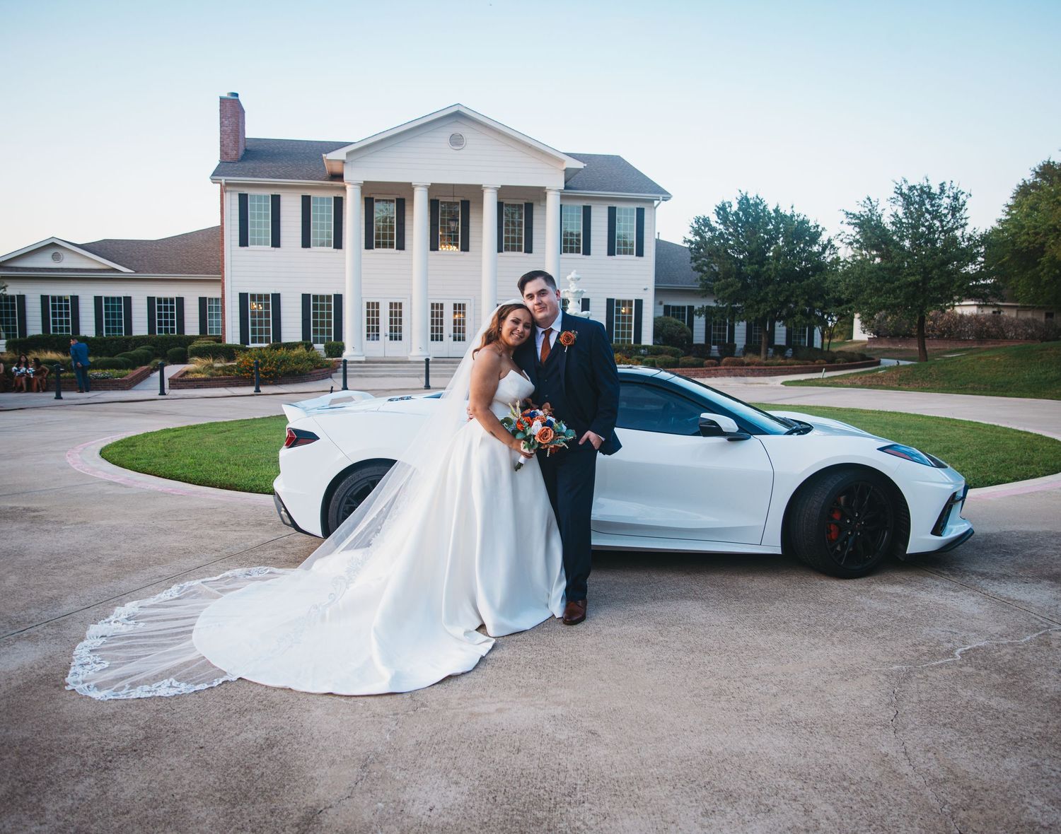 Wedding photo series with luxury car featuring elegant white dress trailing along driveway.