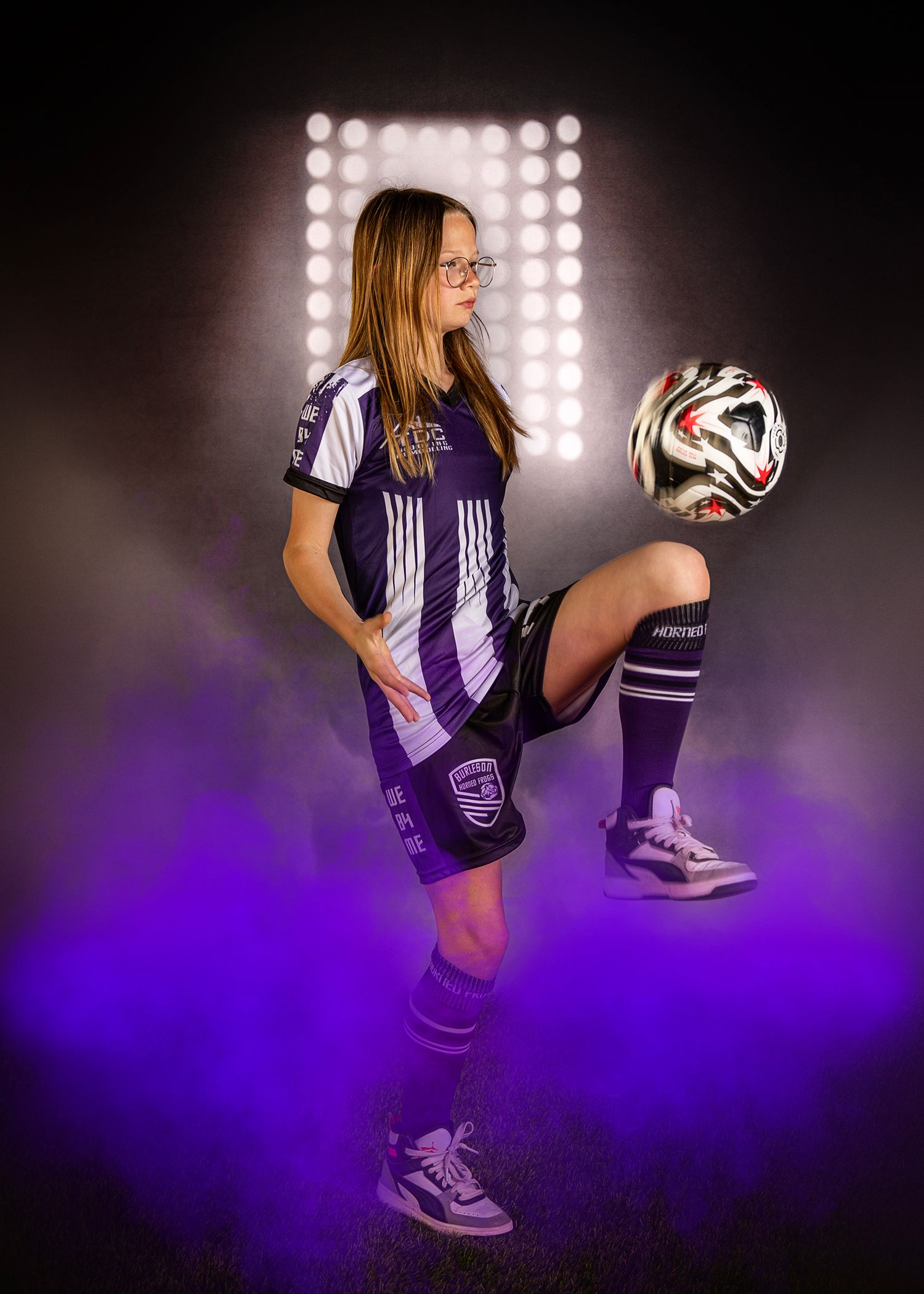 Sports-themed photo shoot with purple lighting and soccer ball against dark background.