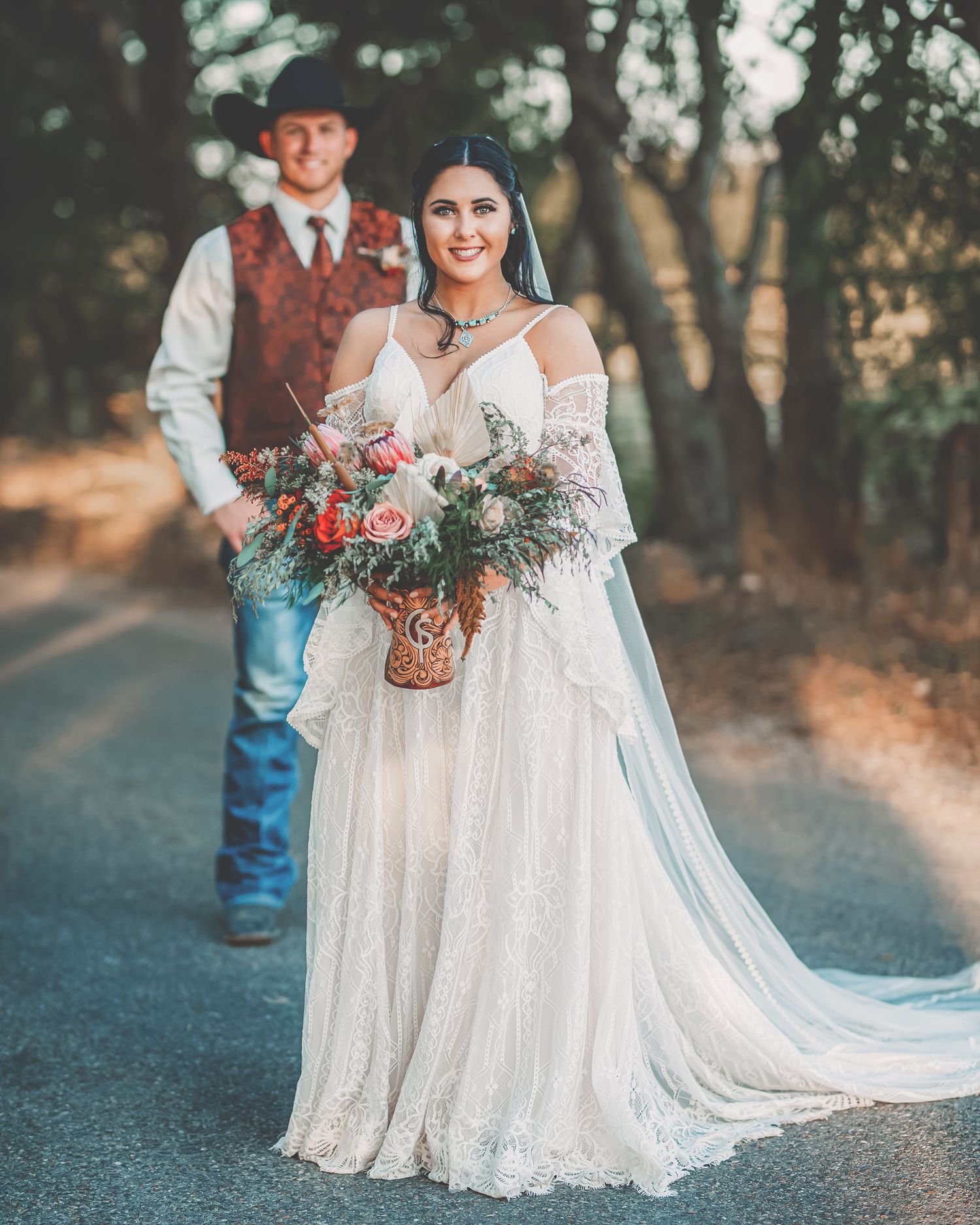 Rustic wedding photo with lace dress and floral bouquet on forest path.