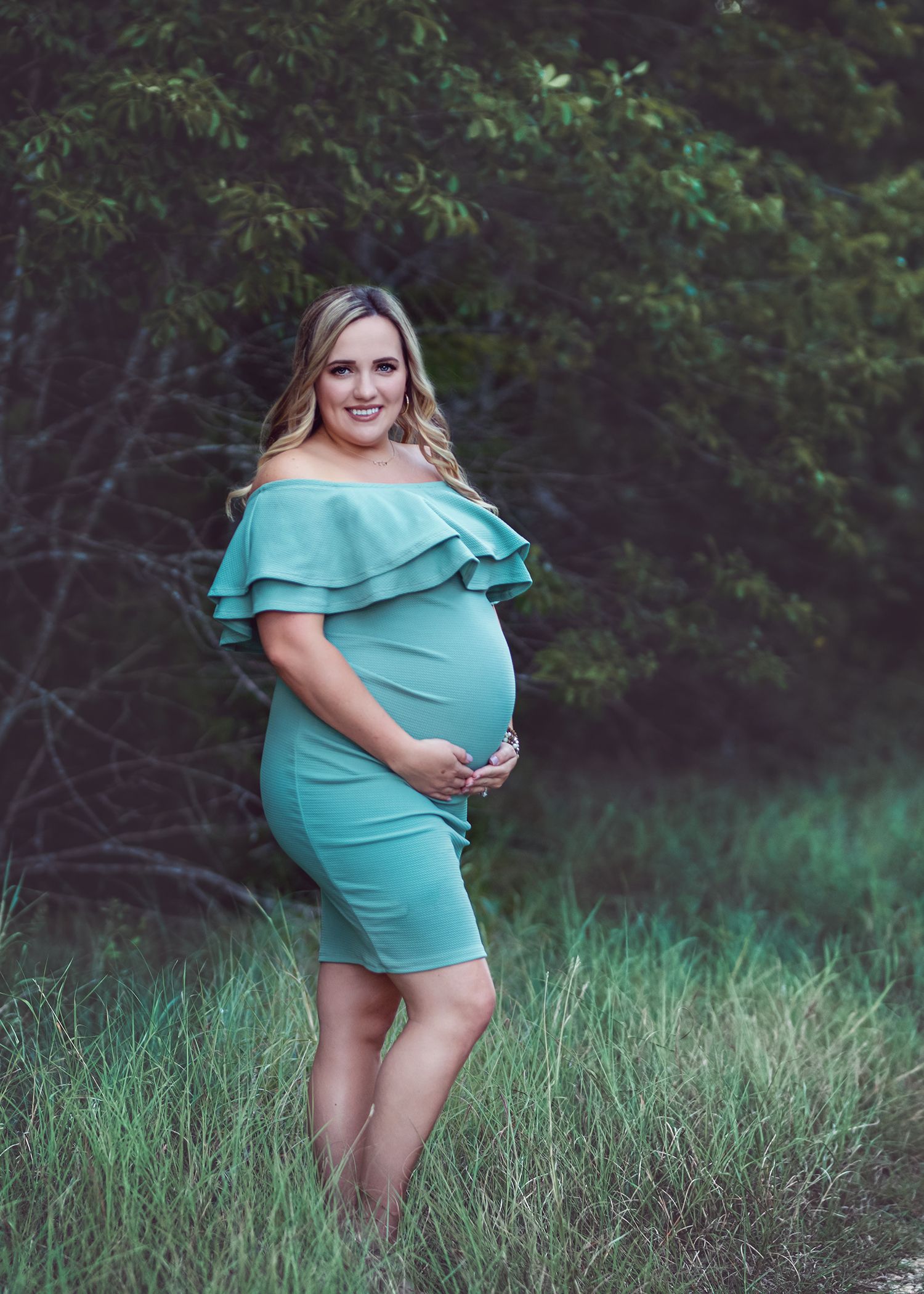 Maternity photoshoot in turquoise dress against natural outdoor setting.