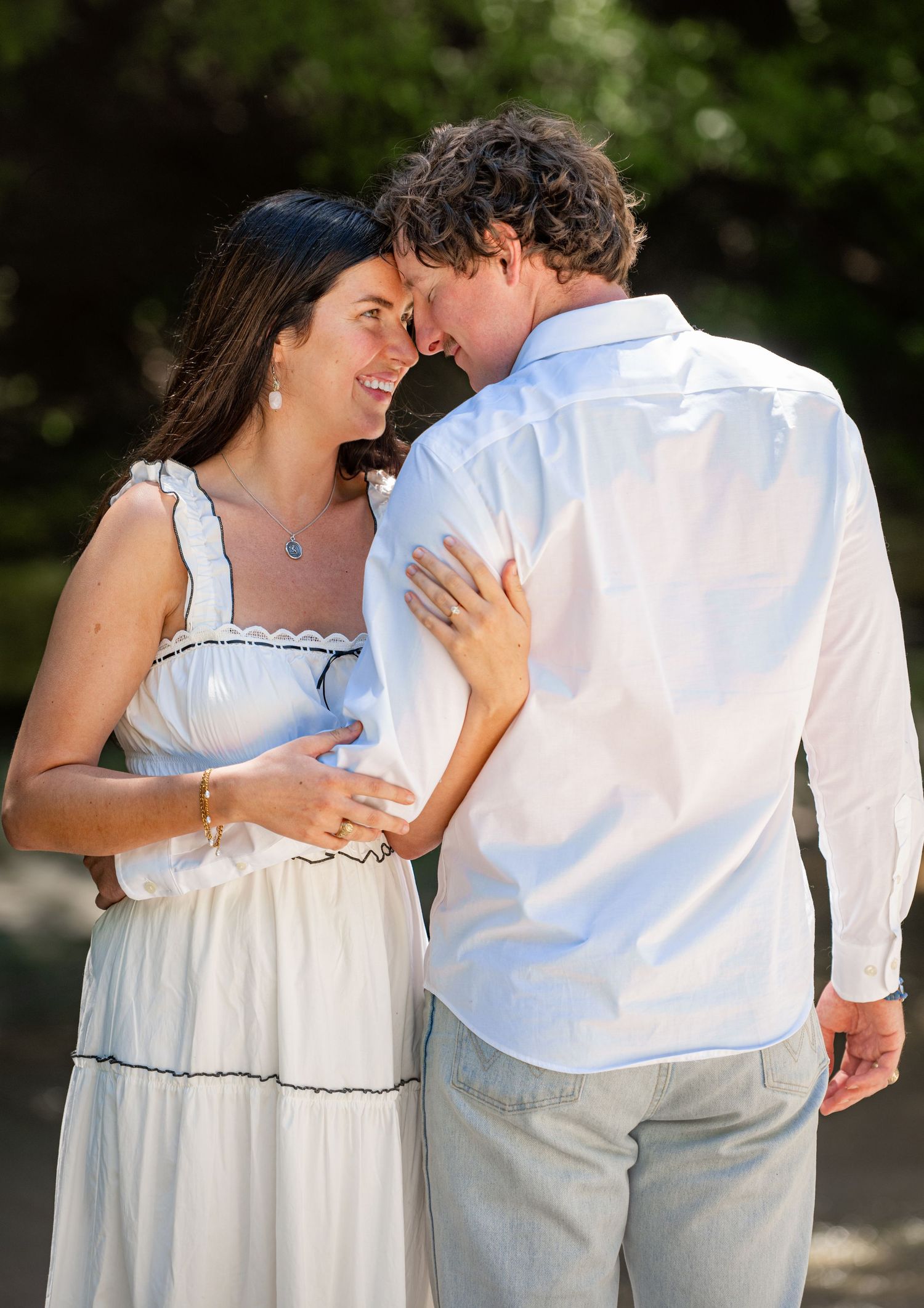 A couple in white clothing shares a tender moment while embracing in a sunlit garden setting.