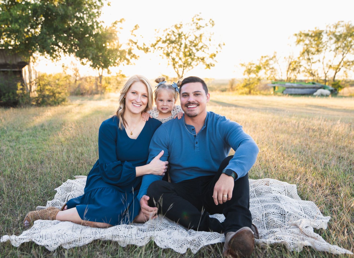 Family of three sits on blanket during golden hour outdoor photo session.