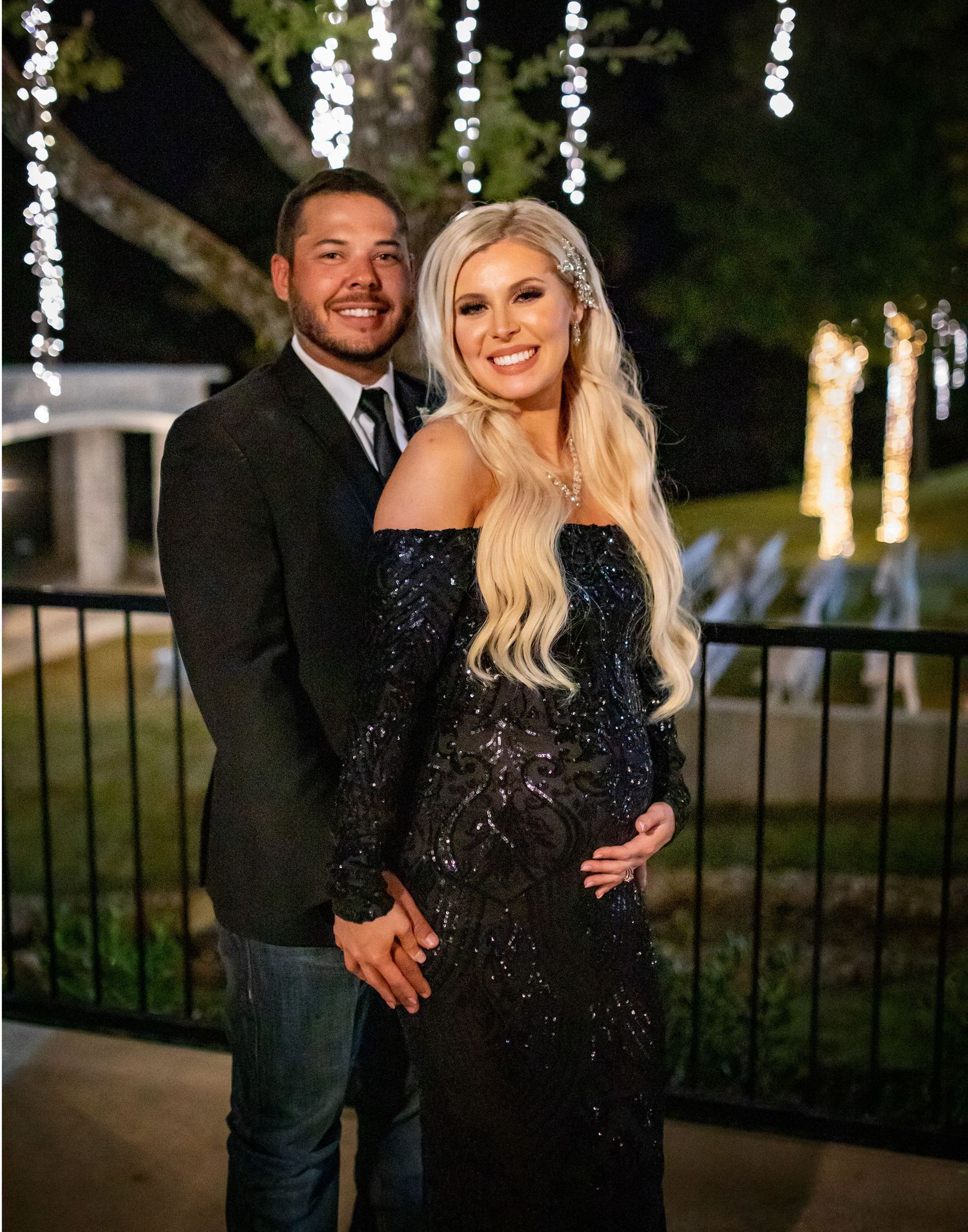 Couple embracing outdoors at night with twinkle lights in the background.