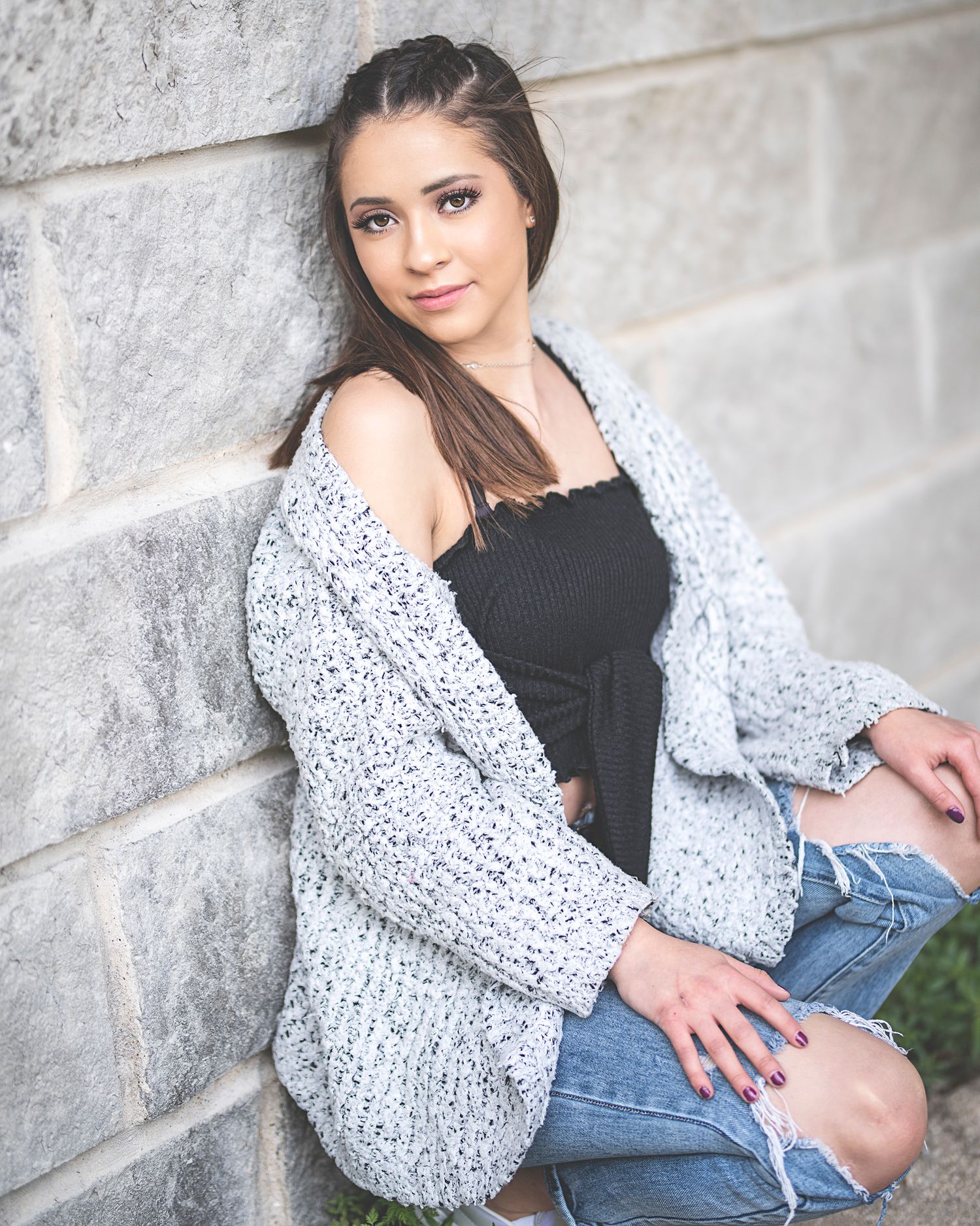 Series of casual senior portraits against stone wall showcasing fashionable winter outfit.