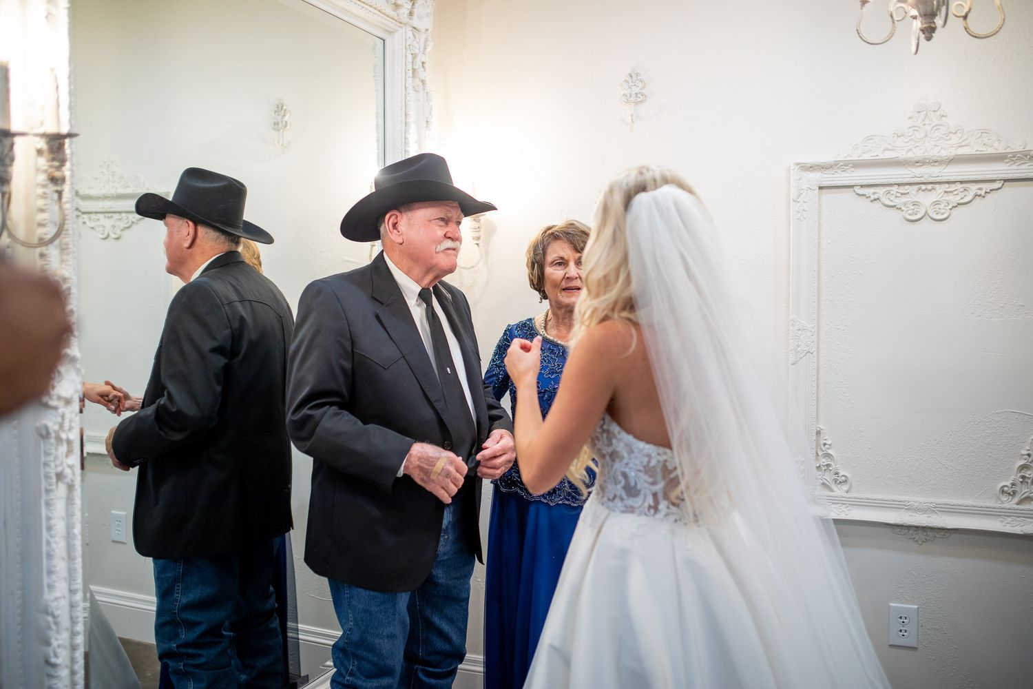 Wedding party preparing in a white-walled room with men in black cowboy hats and a bride in a flowing gown.
