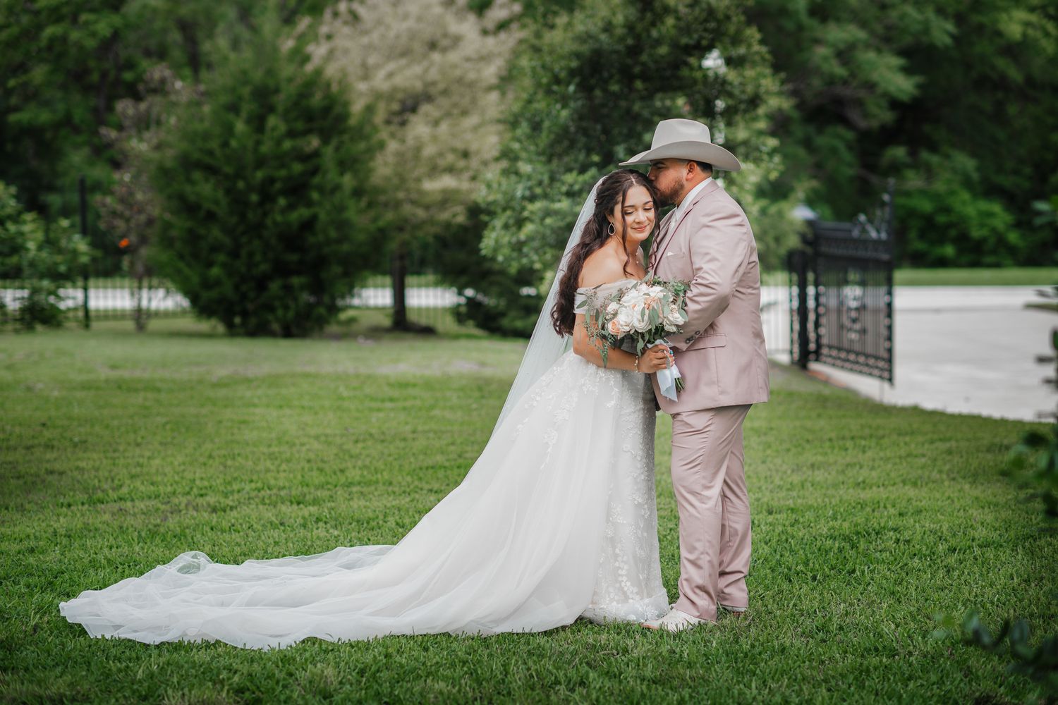 A wedding couple poses on a lawn with a flowing white dress and dusty pink suit.