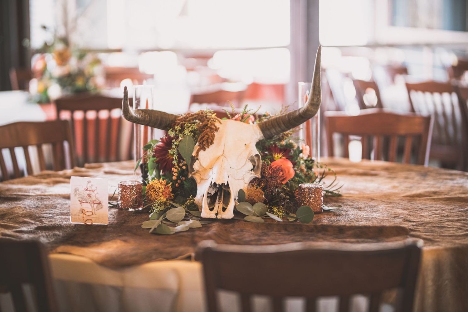 Western-themed table centerpiece with deer skull and floral arrangement on lace tablecloth.