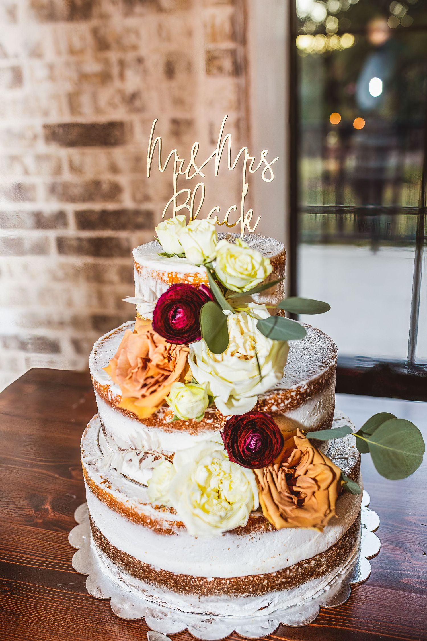Elegant three-tier naked wedding cake decorated with roses and custom Mr & Mrs topper.