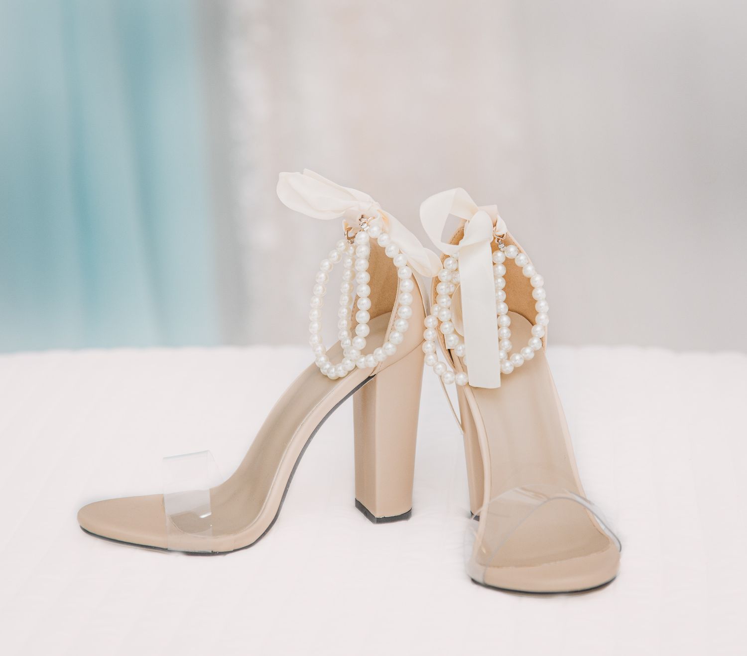 Elegant beige high heels with pearl straps displayed against a light background.