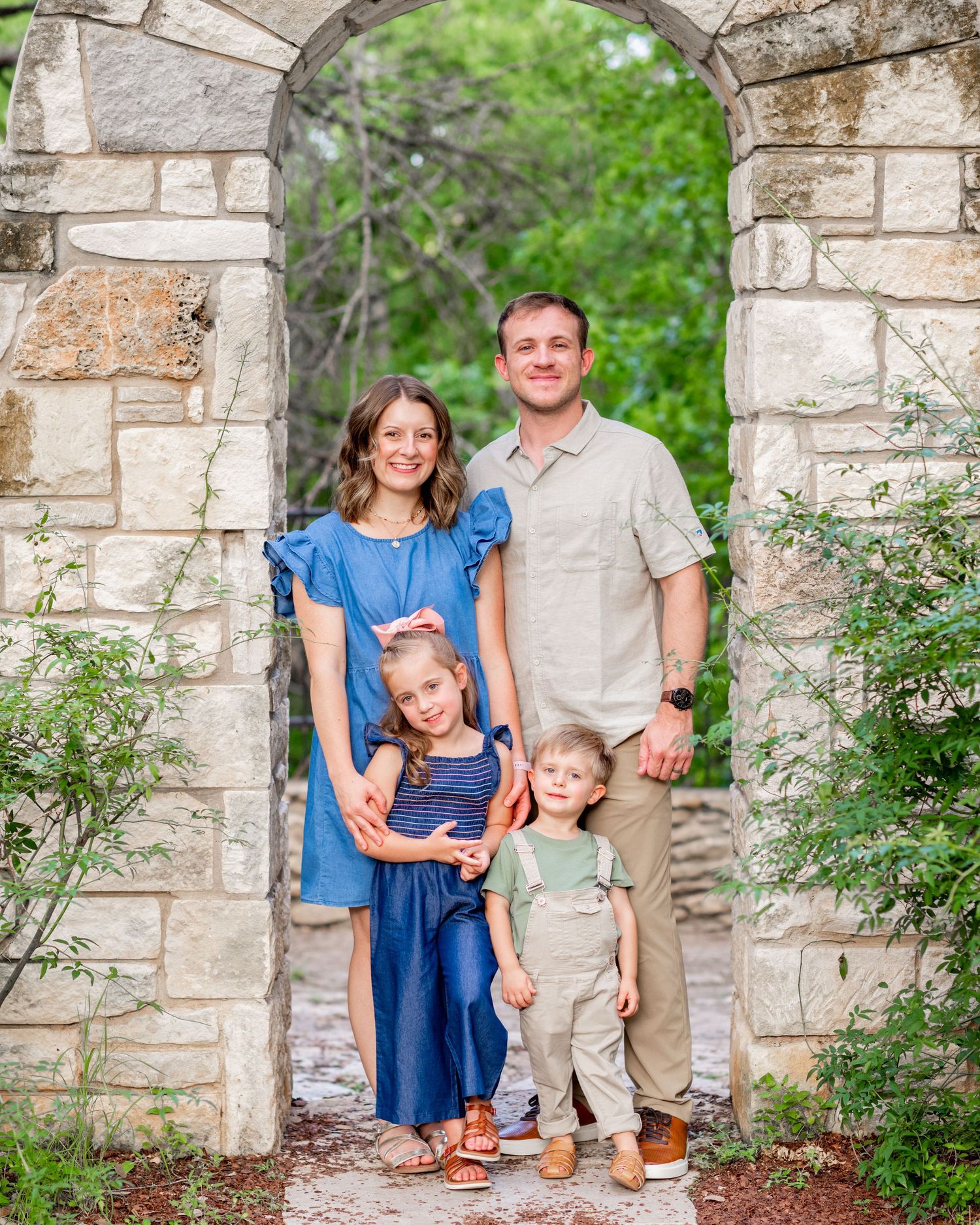 Family portrait session under stone archway with natural greenery.