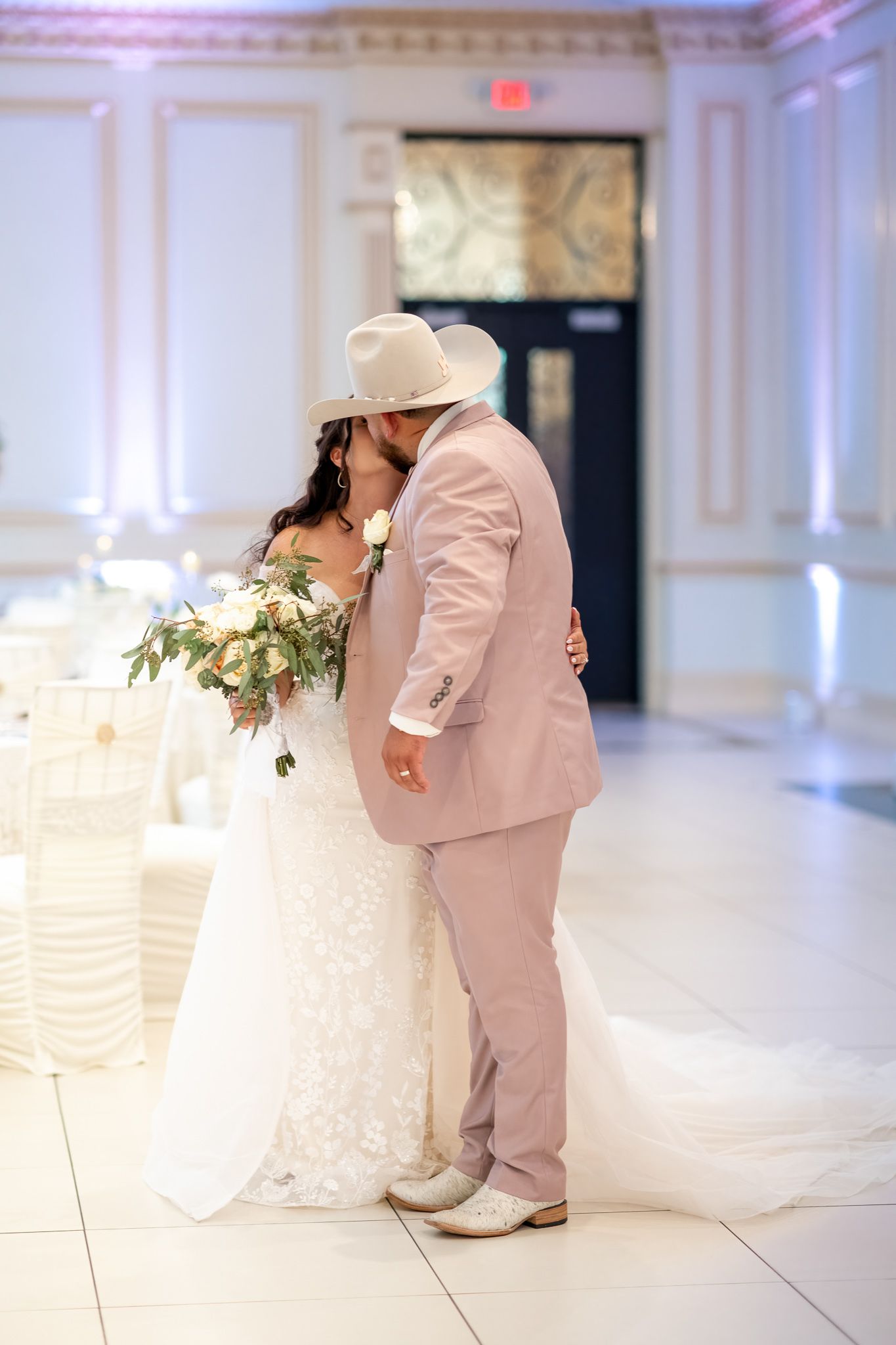 A romantic wedding moment with the couple in white dress and pink suit on a white dance floor.