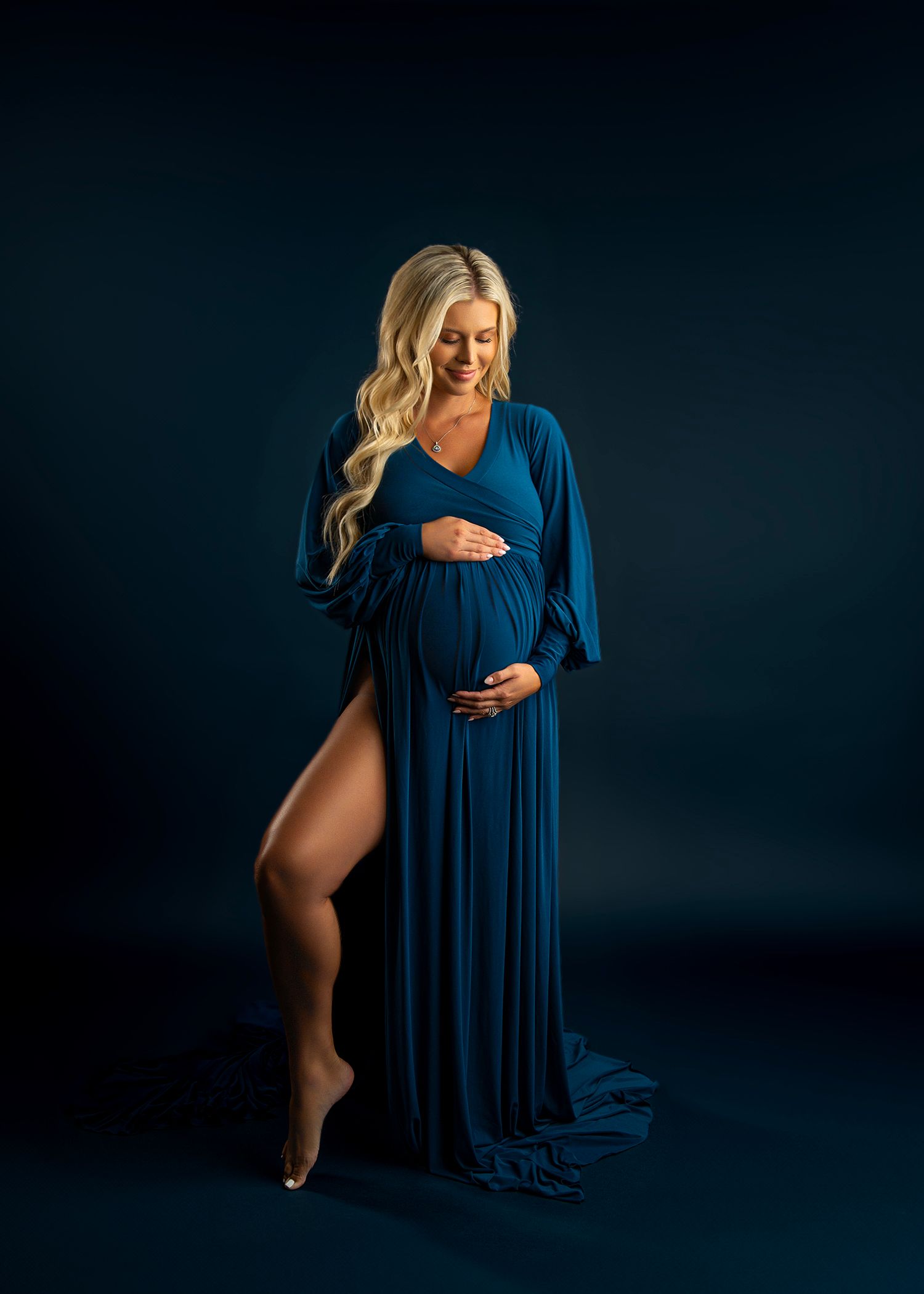 Artistic maternity studio portraits featuring flowing navy blue gown against dark backdrop.
