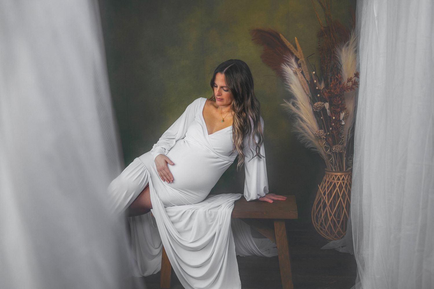 A bride in a flowing white wedding dress poses in an outdoor garden setting with natural lighting and white drapes.