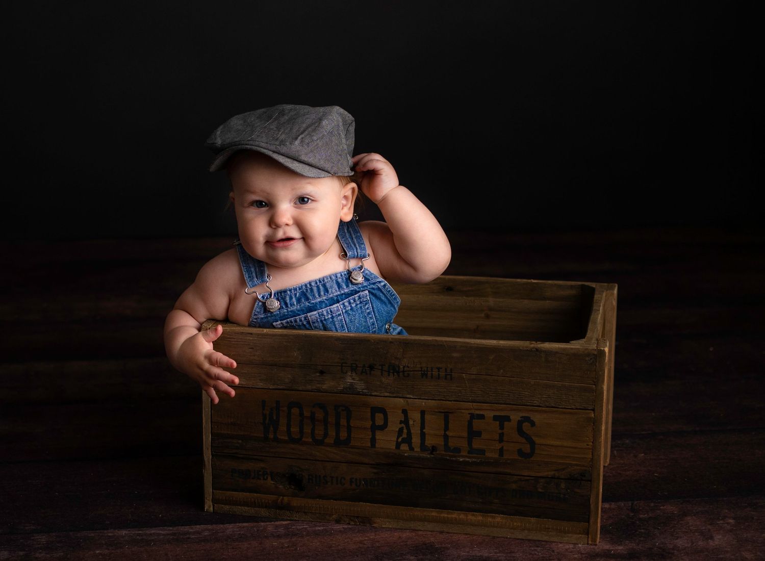 Baby photo series showing playful poses with vintage wooden crates against black background.