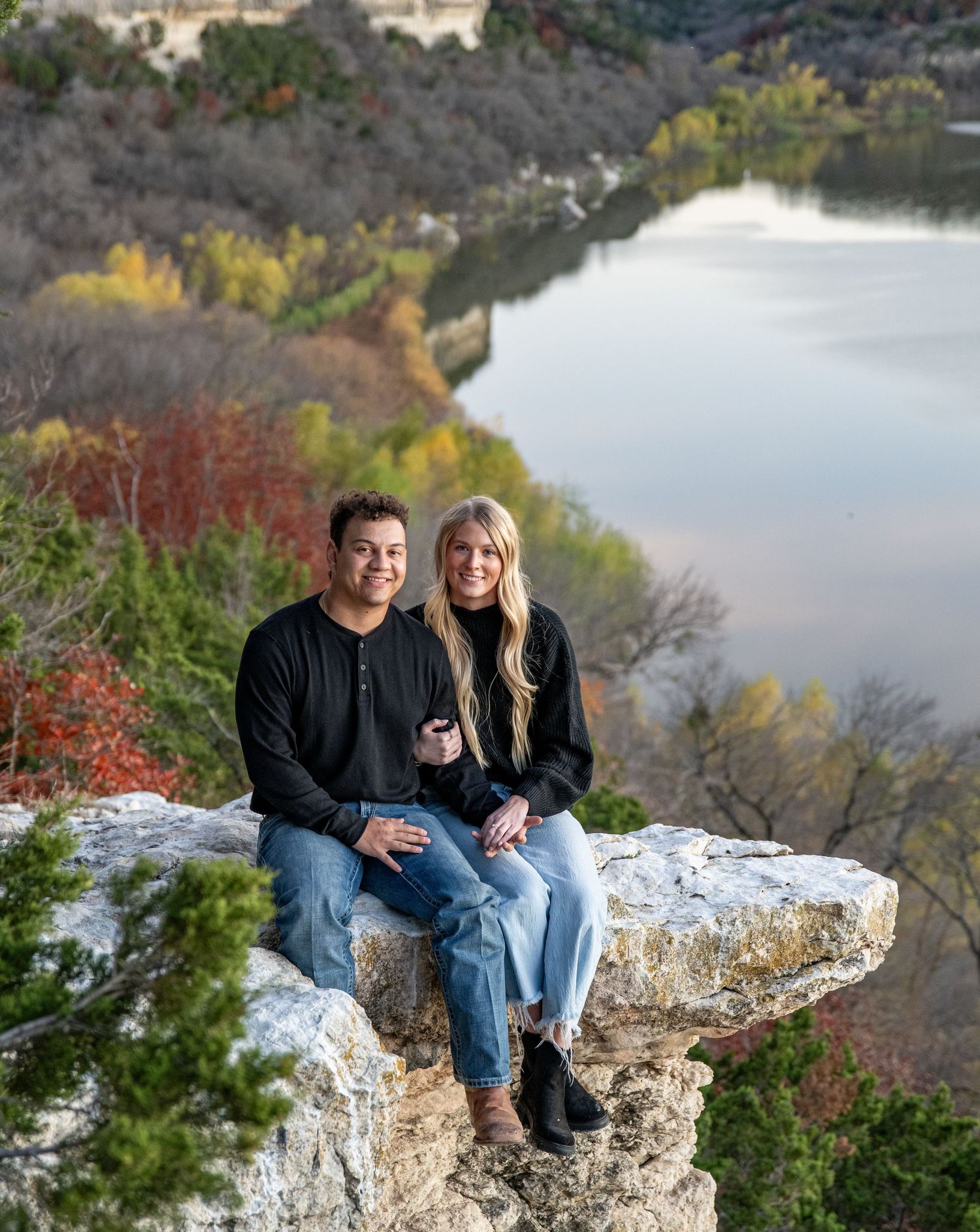 Couple enjoying scenic view from limestone cliff above autumn-colored lake.