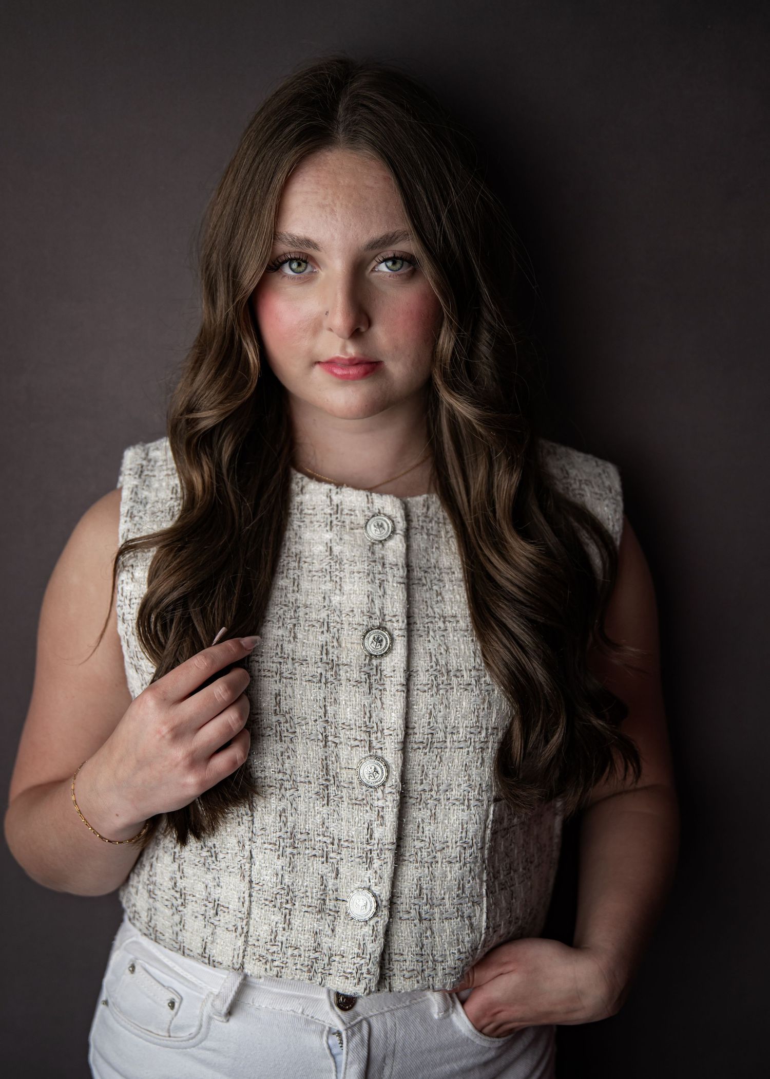 Studio portrait features person in textured white button-up vest against dark background.