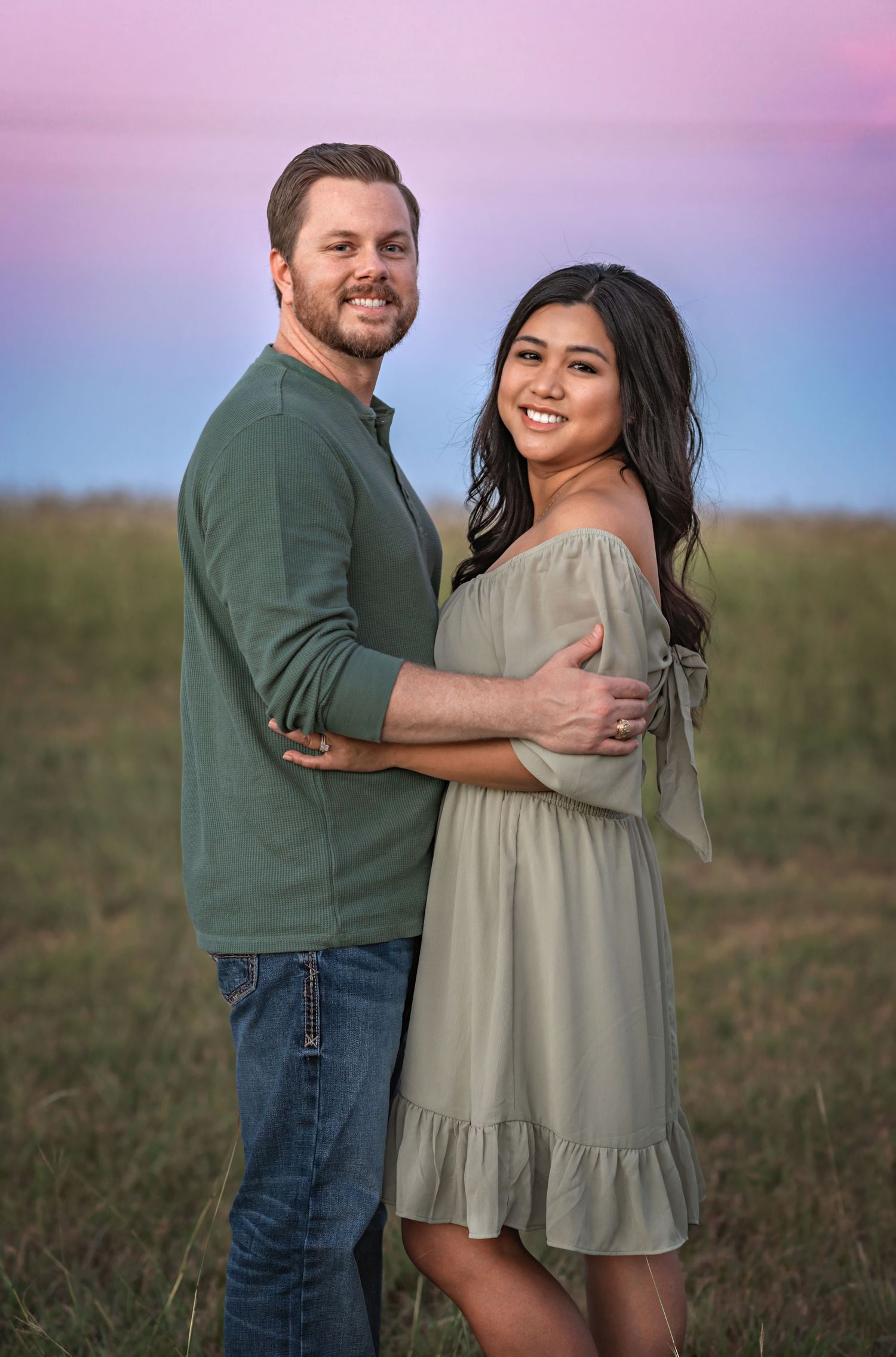 Couple embraces in casual attire against sunset backdrop during outdoor portrait session.