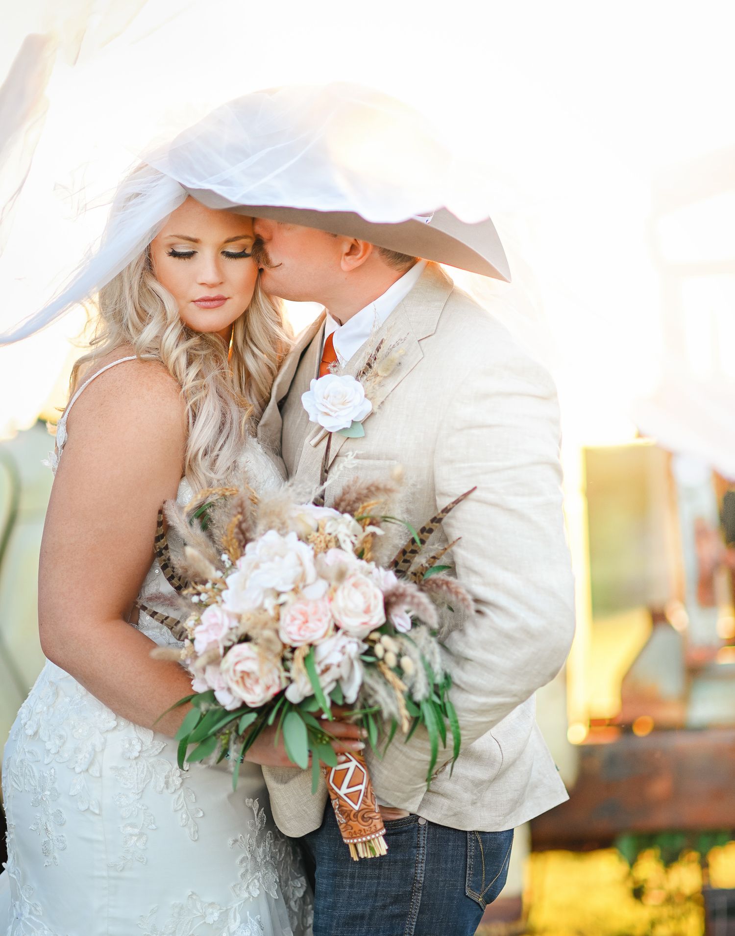 A romantic wedding portrait under a white veil with a blush and white floral bouquet.