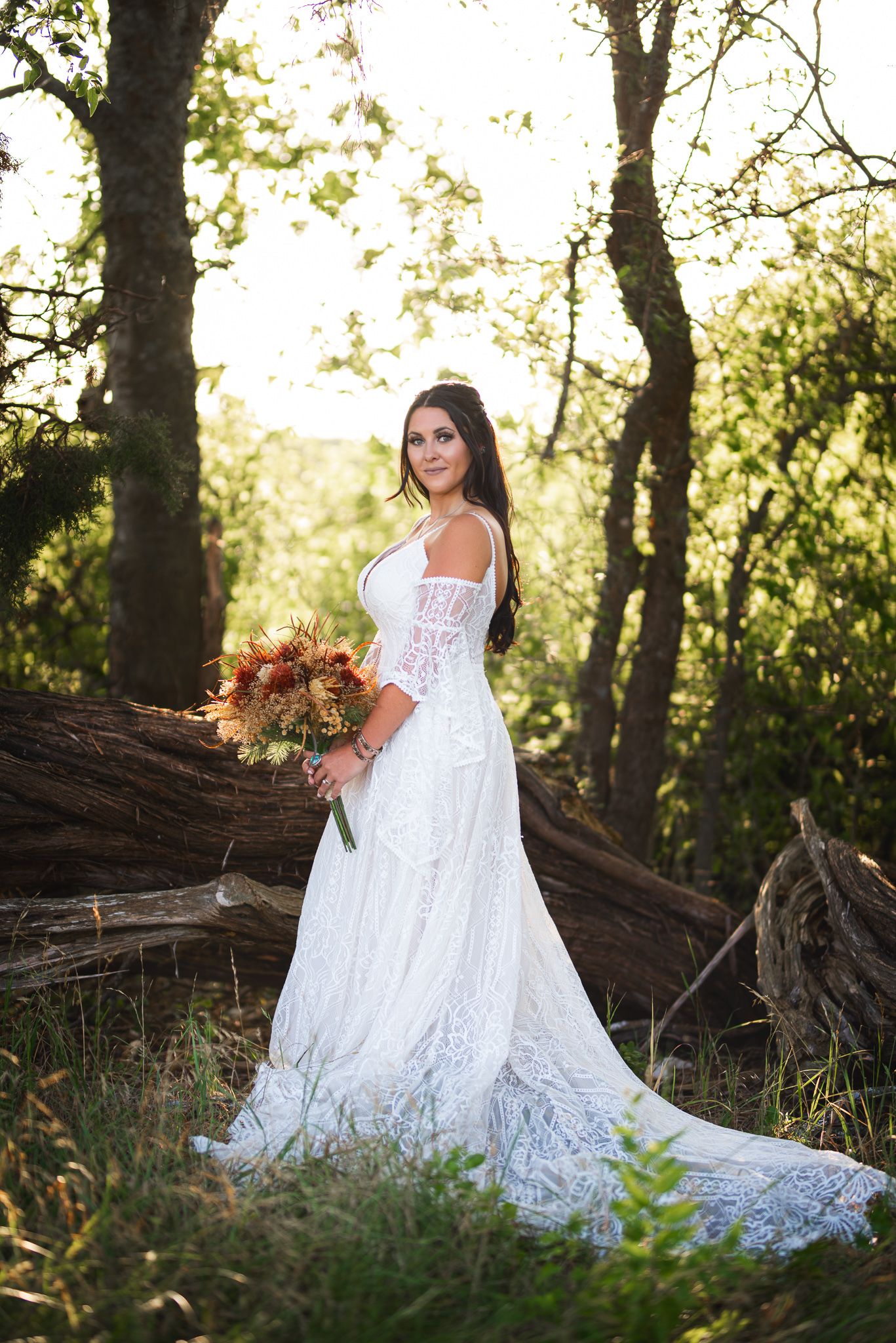 Elegant white lace gown with train photographed in a wooded setting with fall bouquet.