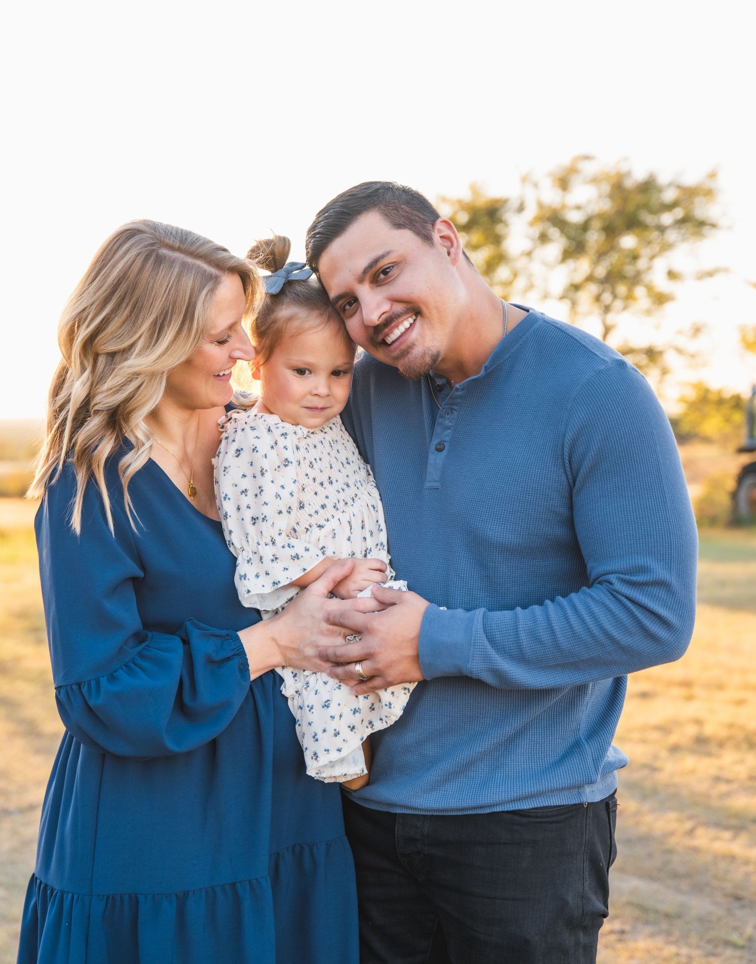 A family shares a tender moment together at sunset in an outdoor field setting.