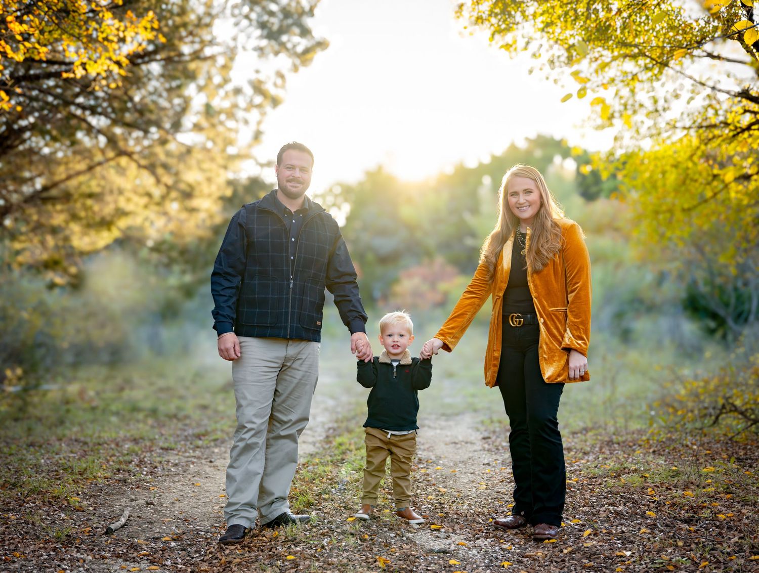 Candid family moments captured on autumn trail with golden sunlight filtering through trees.