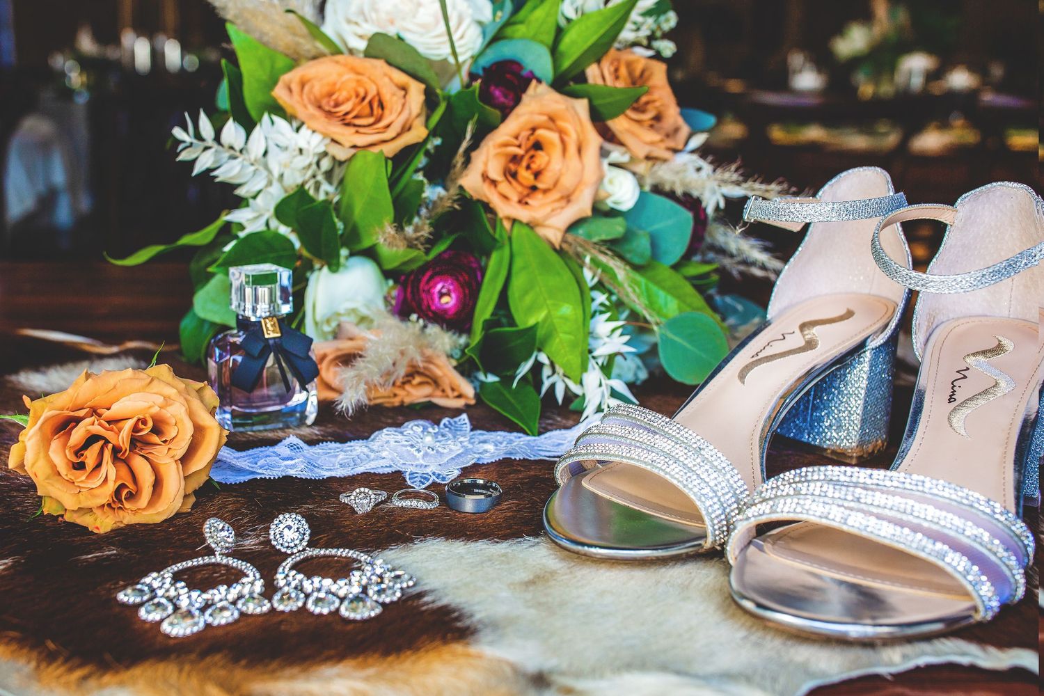 Wedding accessories including champagne glasses, roses, and bridal jewelry displayed on dark wood.