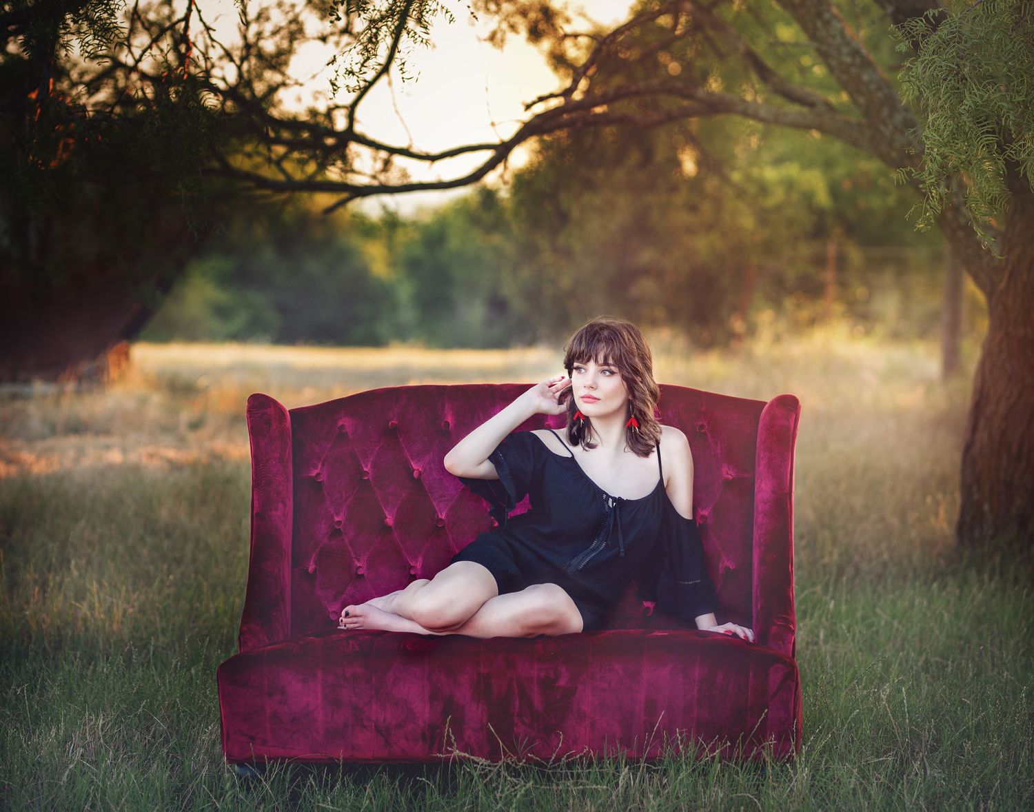 Portrait session on vintage burgundy velvet couch in outdoor field setting.