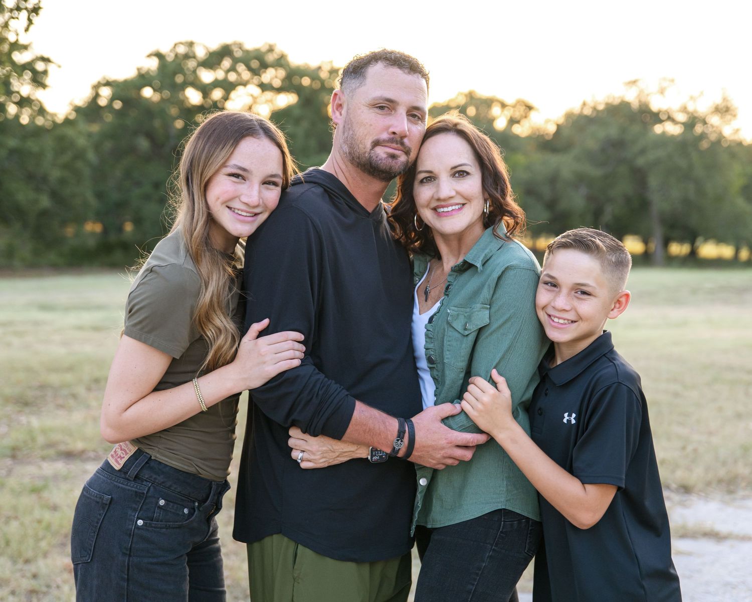 Family portrait outdoors against golden sunset backdrop in coordinated casual outfits.
