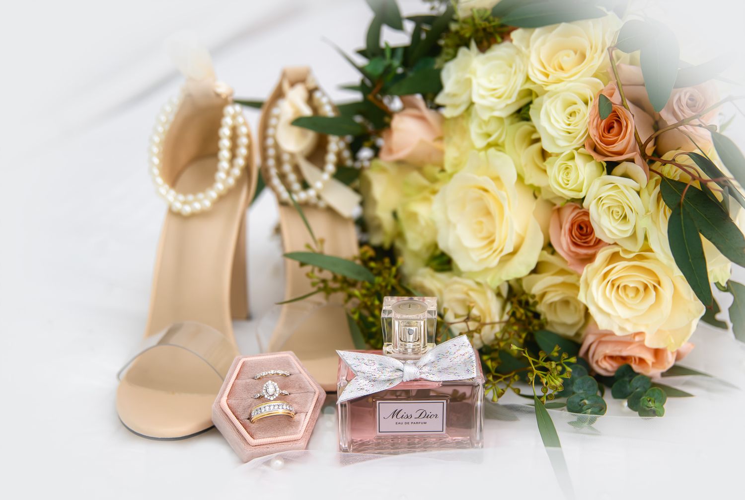 Wedding details including perfume bottles, yellow roses and pearls arranged on a light surface.