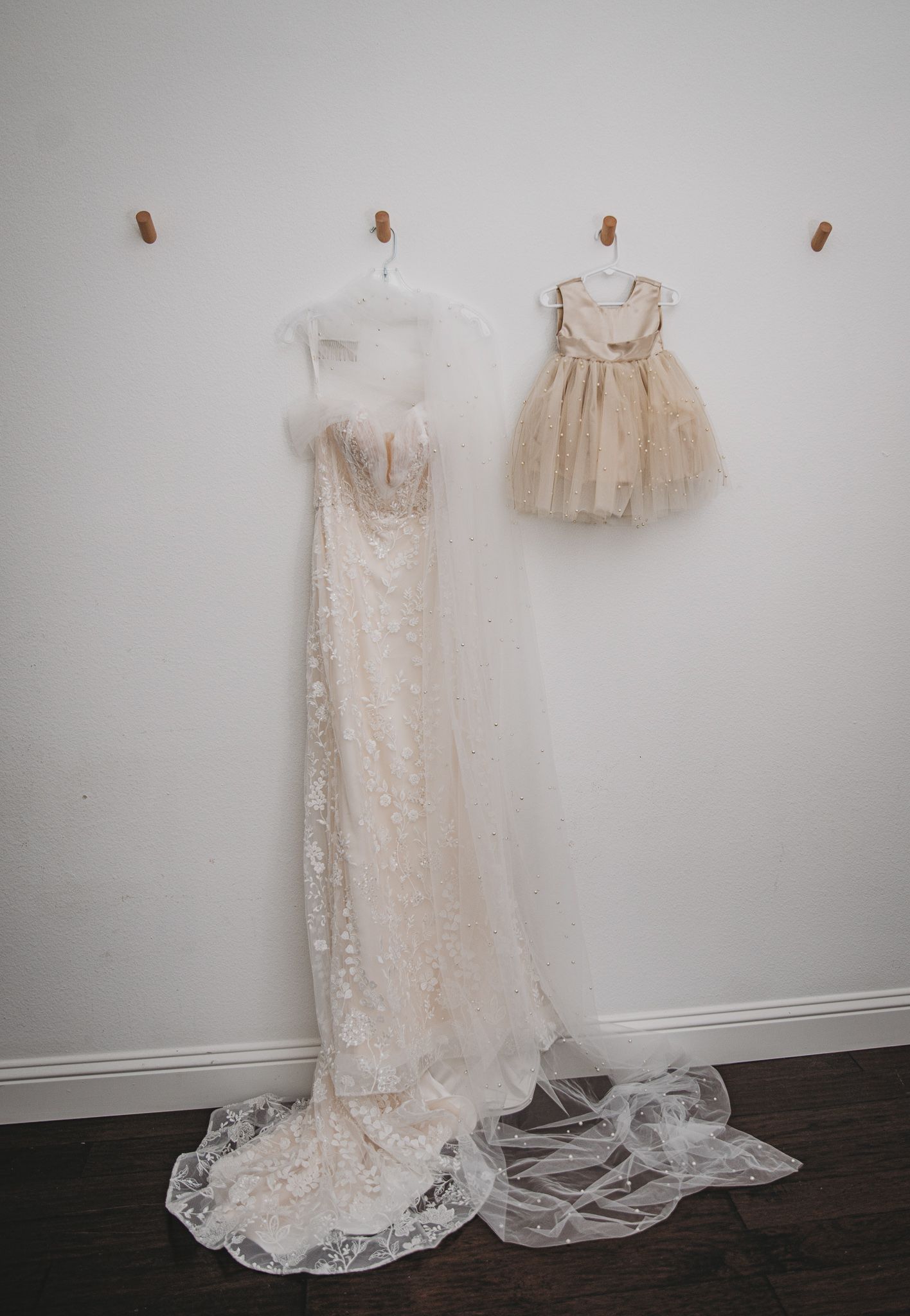 White lace wedding gown and small tulle dress hanging on wall display for mother and daughter set.