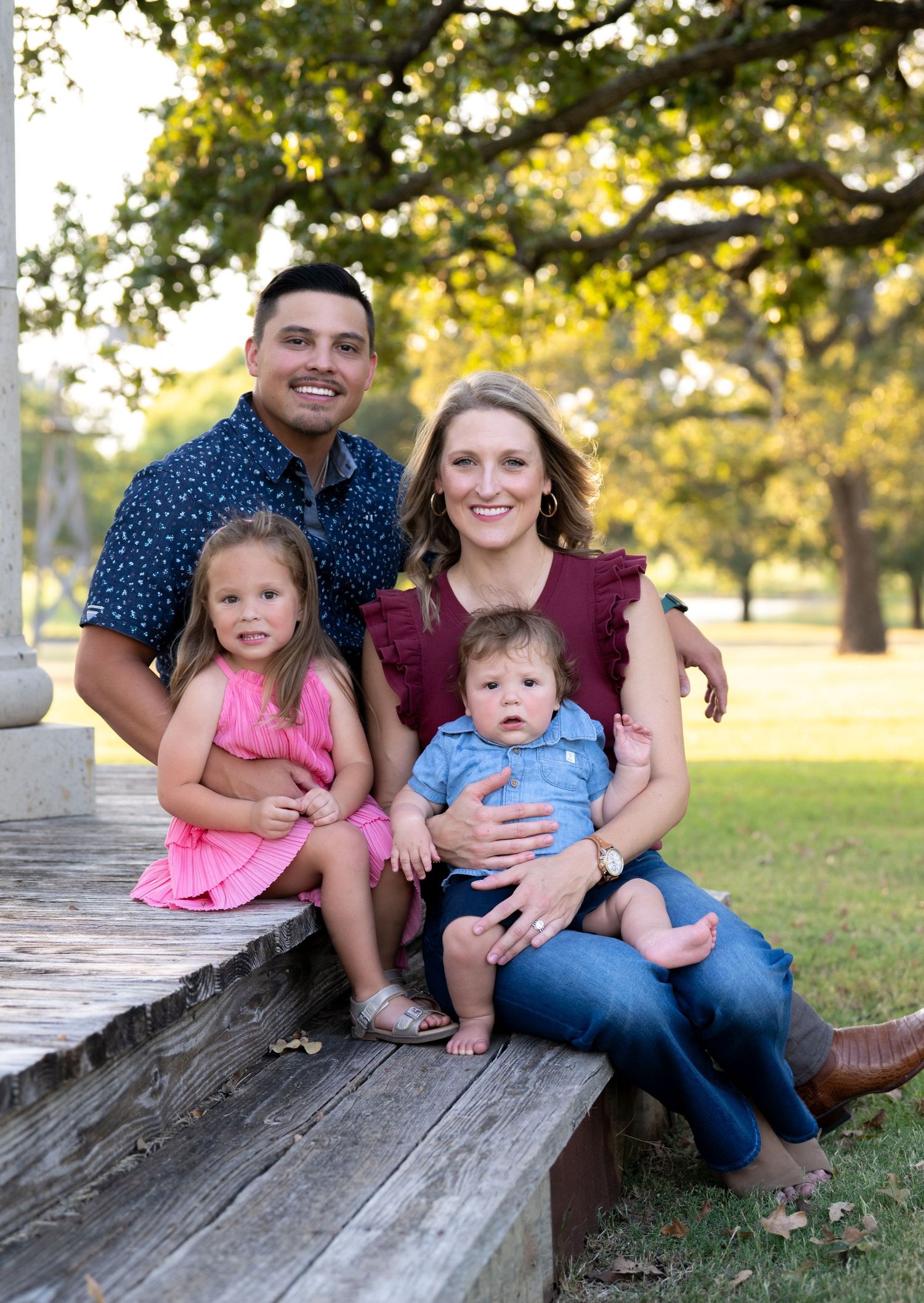A family sits together on rustic wooden steps in a park setting during golden hour.